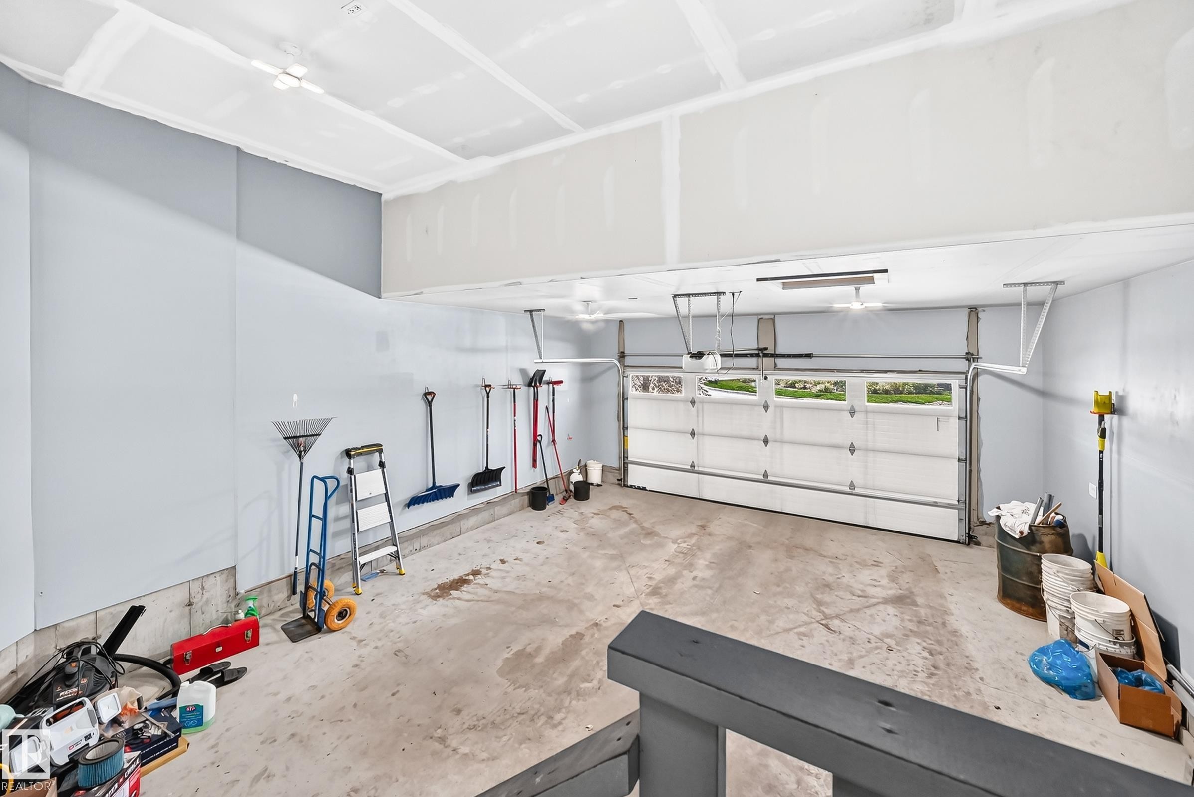 Spacious garage with exposed beam ceiling, light-toned walls, concrete flooring, and a white paneled garage door with upper window inserts - 1781 Melrose Crescent, Edmonton, AB
