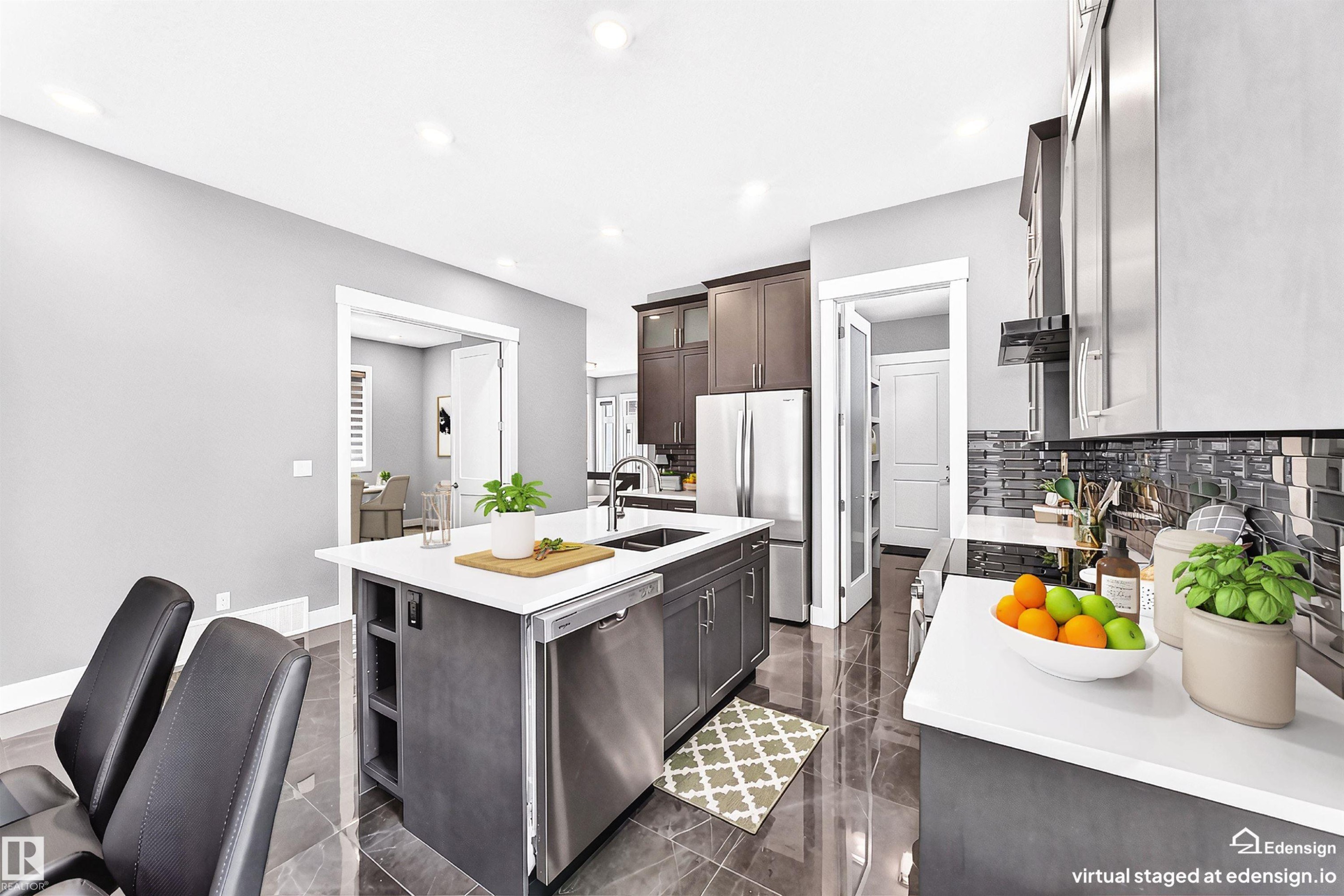 Contemporary kitchen featuring an expansive center island with an undermount sink, stainless steel appliances, dark wood-finish cabinetry, white countertops, and a subway tile backsplash - 1781 Melrose Crescent, Edmonton, AB