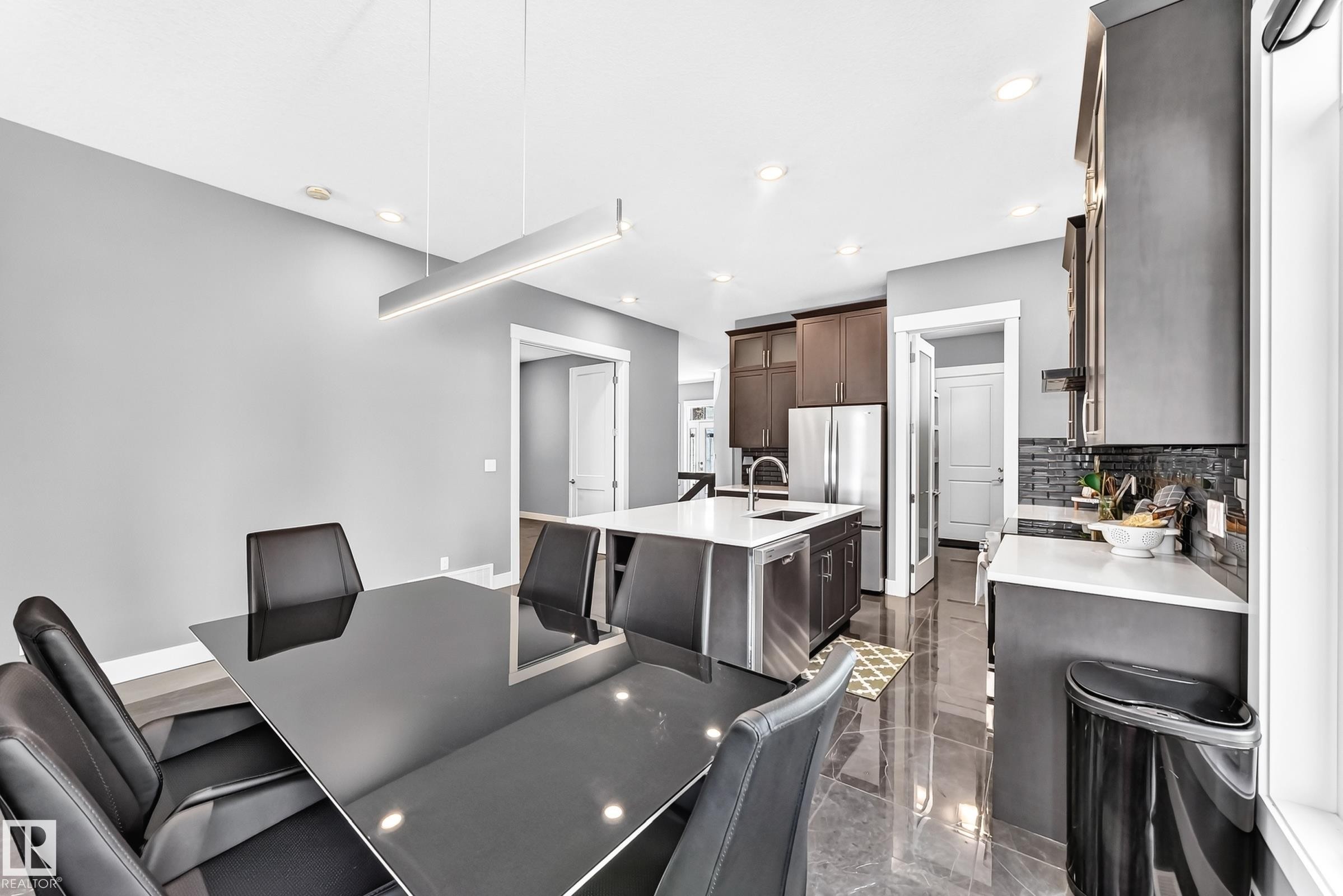 Spacious dining area featuring a modern linear pendant light and a sleek black table - 1781 Melrose Crescent, Edmonton, AB