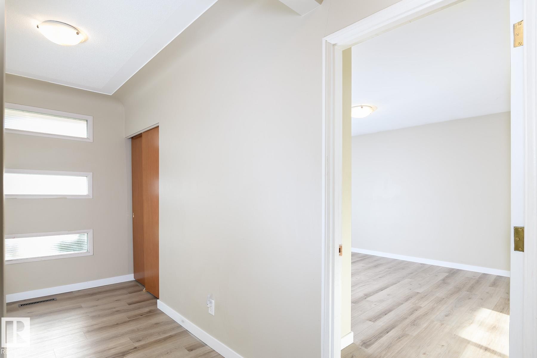 Entryway featuring light wood-finish flooring, three horizontal translucent windows, a built-in wood-finish sliding door, and a flush-mount ceiling light fixture - 9607 75 Street, Edmonton, AB