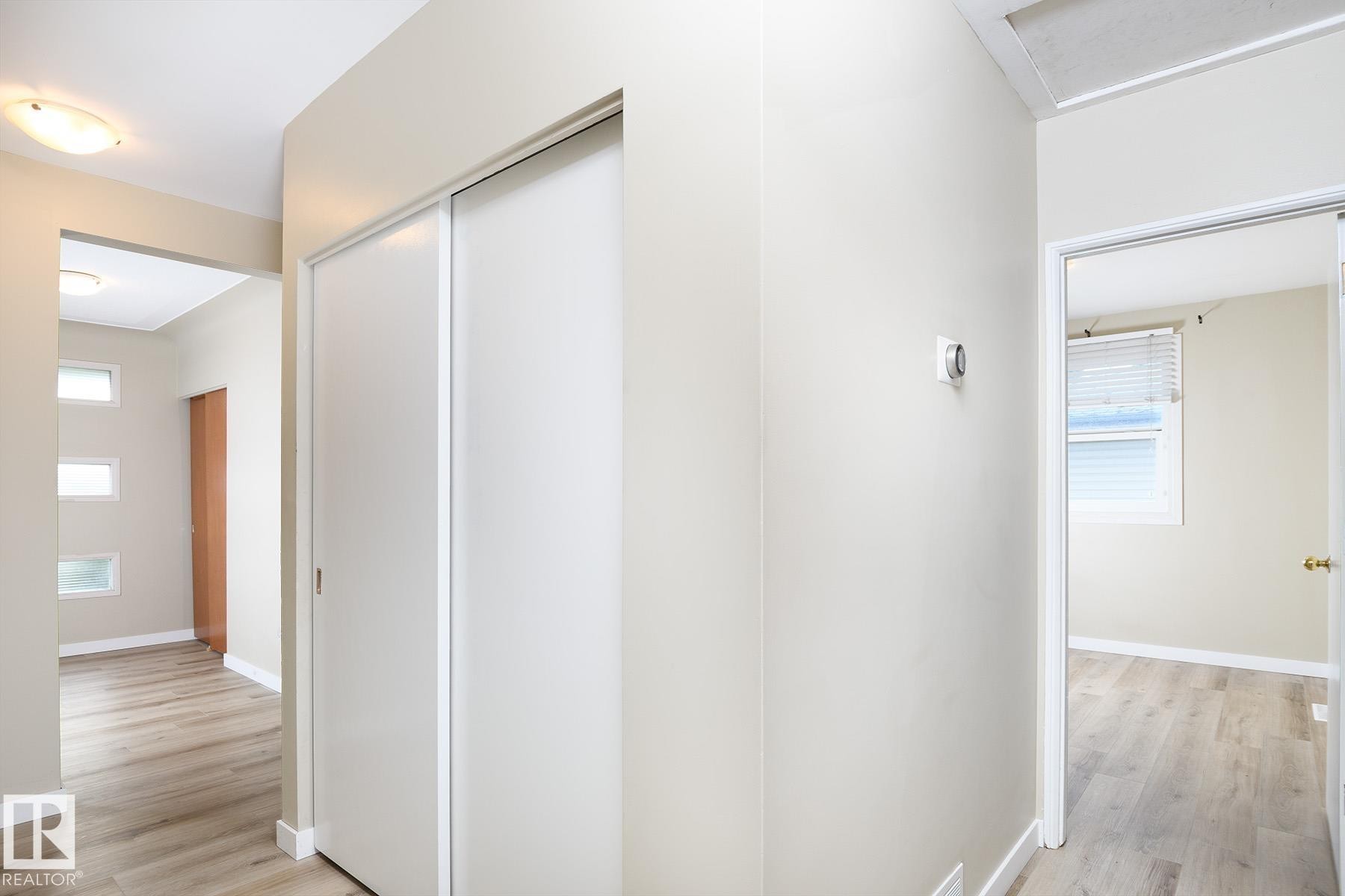 Hallway featuring wood-finish flooring, white sliding closet doors, and recessed lighting - 9607 75 Street, Edmonton, AB