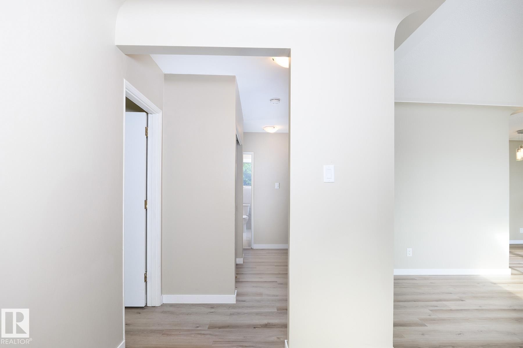 Expansive interior hallway featuring light-colored walls, wood-finish flooring, white baseboards, and recessed lighting - 9607 75 Street, Edmonton, AB