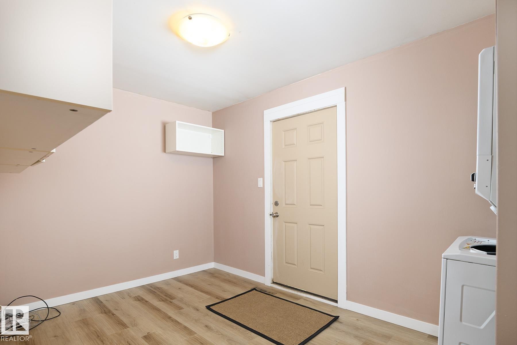 Interior space featuring wood-finish flooring, a six-panel door with white trim, and a flush-mount ceiling light - 9607 75 Street, Edmonton, AB