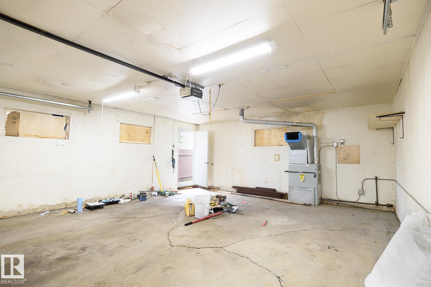Spacious garage featuring a concrete floor, built-in shelving brackets, fluorescent lighting, and visible HVAC system - 9607 75 Street, Edmonton, AB