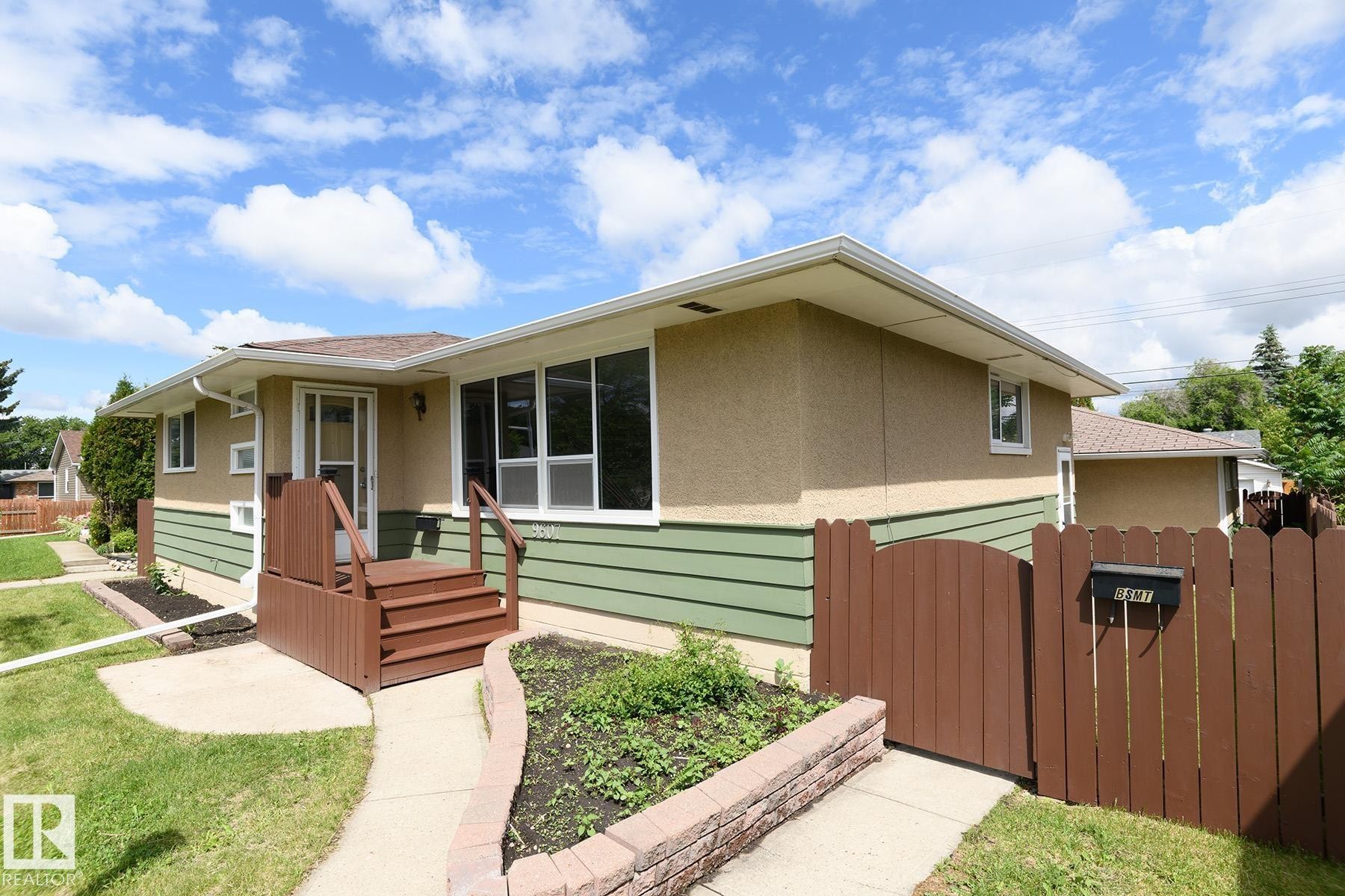 Exterior featuring a combined stucco and horizontal siding facade, a front wooden deck with steps and railings, and a privacy fence with a gate - 9607 75 Street, Edmonton, AB