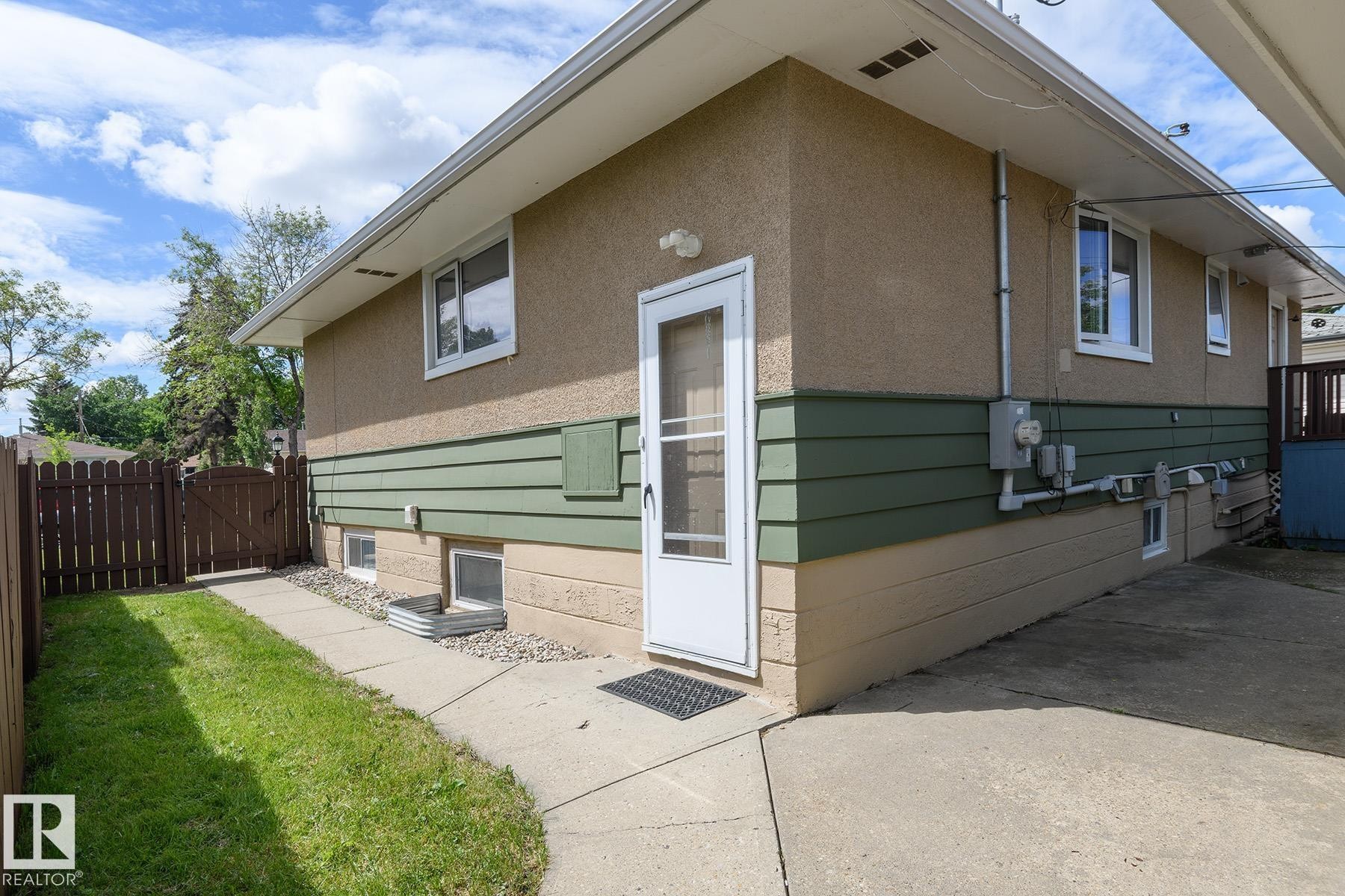 Exterior featuring multi-toned stucco, horizontal siding, multiple windows, a rear entry door, and a brown wood fence - 9607 75 Street, Edmonton, AB