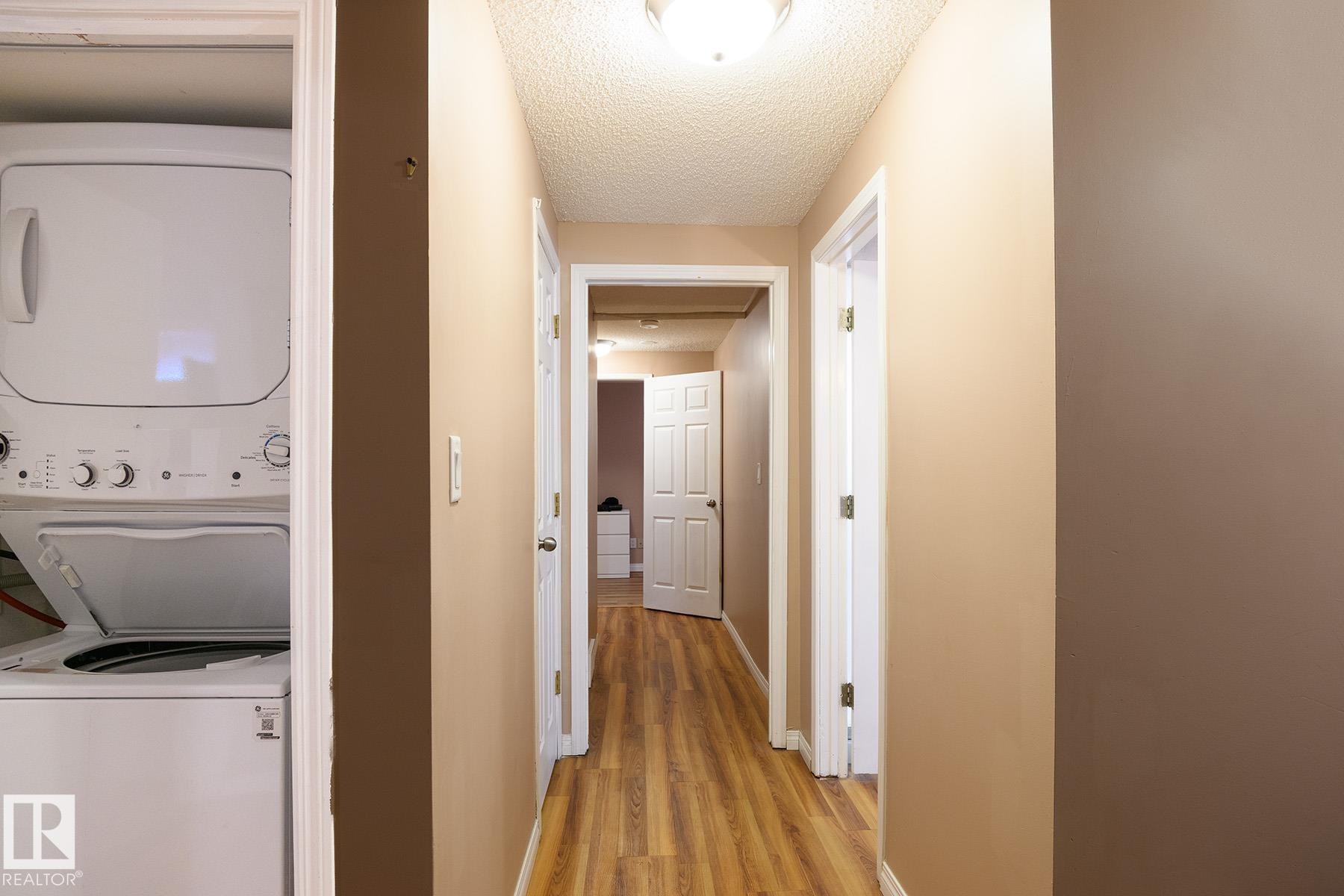 Dedicated laundry closet featuring a stacked washer and dryer, wood-finish flooring, and neutral wall tones - 9607 75 Street, Edmonton, AB