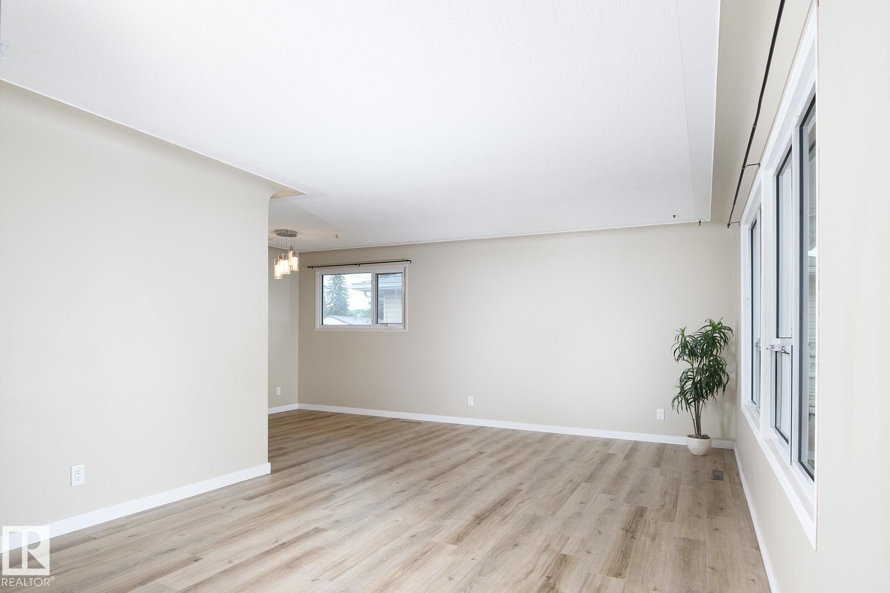 Spacious room featuring light wood-finish flooring, neutral wall tones, white baseboards, and ample natural light from multiple windows - 9607 75 Street, Edmonton, AB