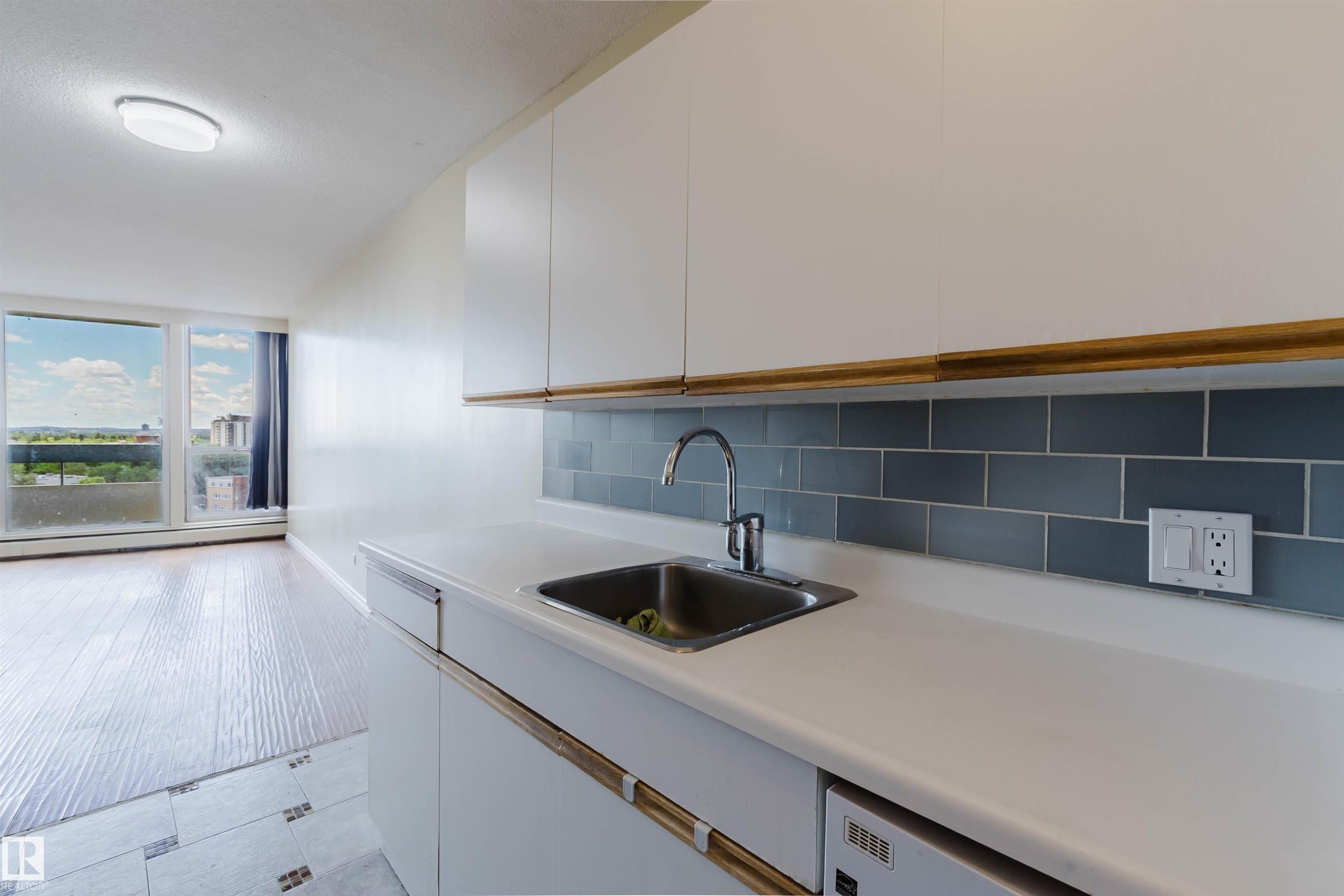 Compact kitchen area featuring white cabinetry, a stainless steel sink, and a gray subway tile backsplash - 904 10883 Saskatchewan Drive, Edmonton, AB