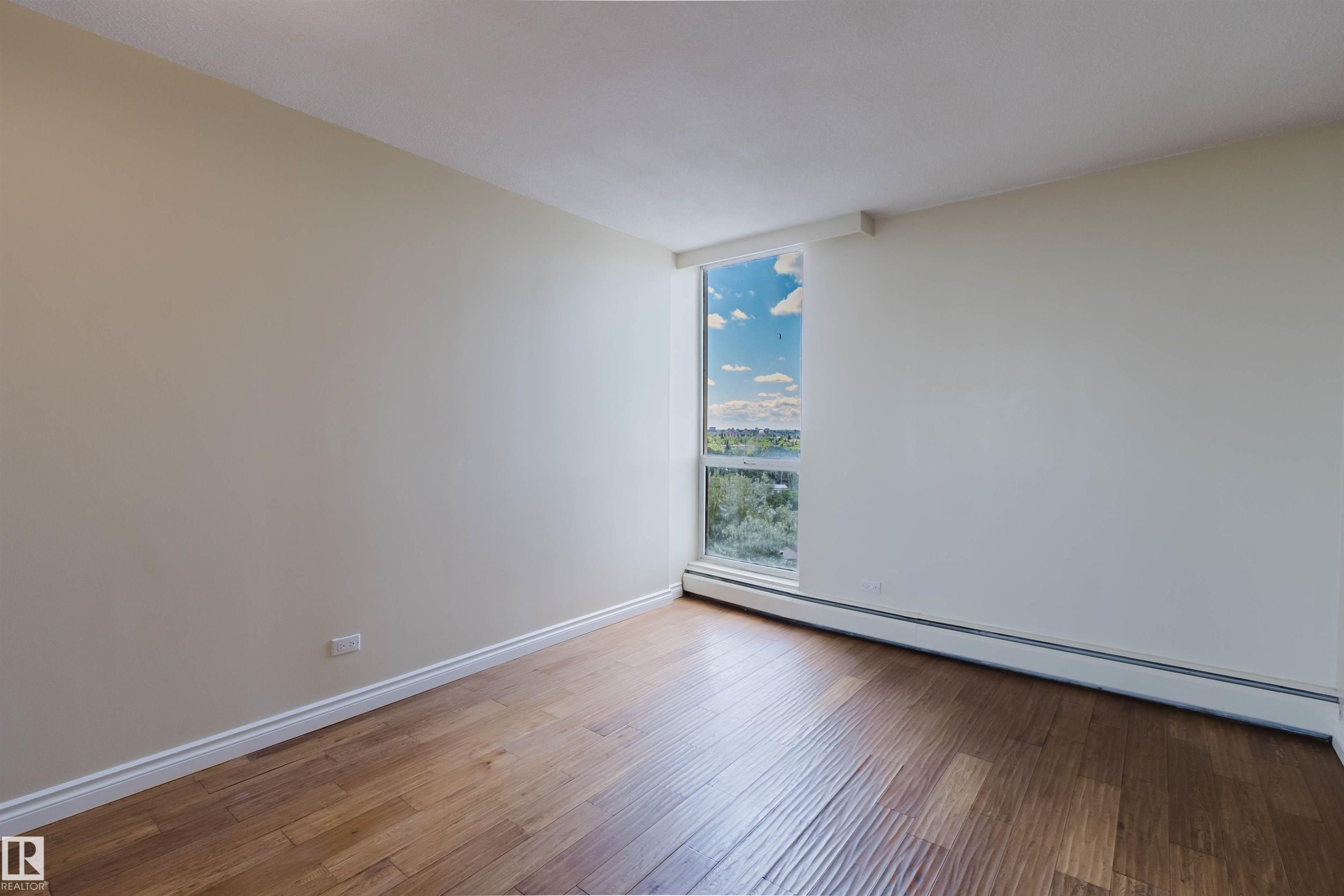 Room featuring a large vertical window, wood-finish flooring, white baseboards, and neutral-toned walls - 904 10883 Saskatchewan Drive, Edmonton, AB