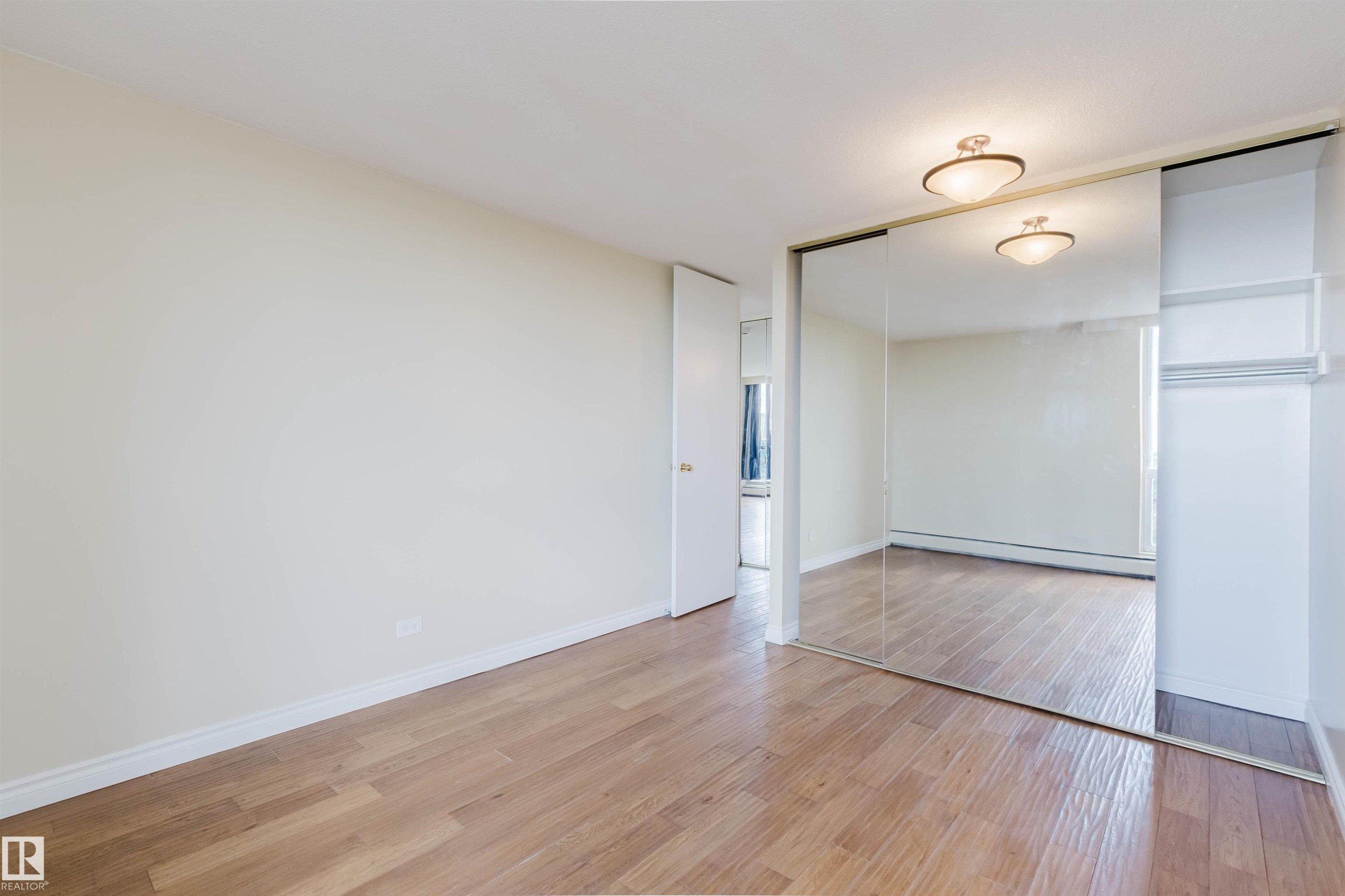 Room featuring wood-finish flooring, white baseboards, and a mirrored sliding closet door - 904 10883 Saskatchewan Drive, Edmonton, AB