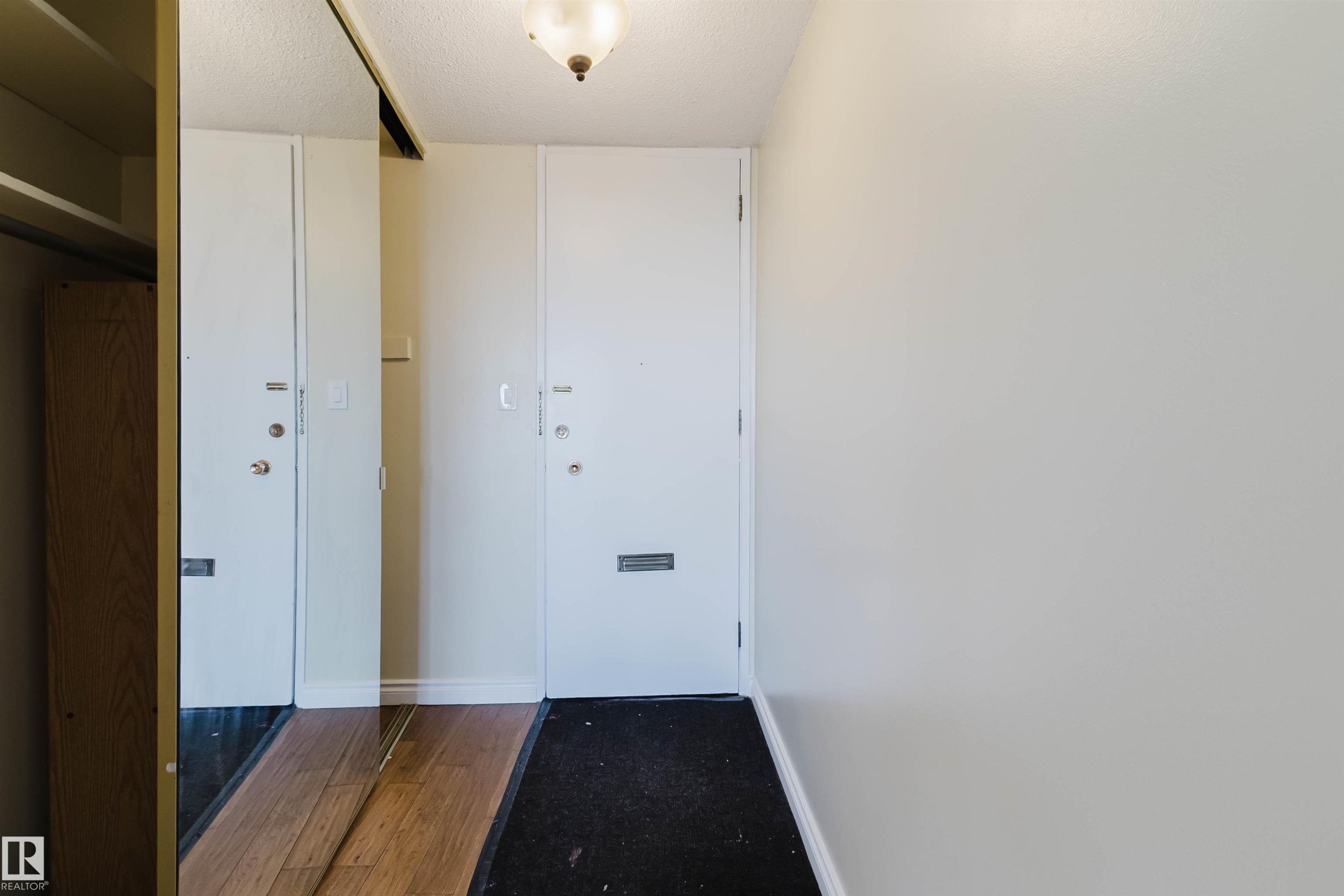 Entryway featuring a white door, overhead light fixture, light-colored walls, and a mirrored closet door with wood-finish flooring reflection - 904 10883 Saskatchewan Drive, Edmonton, AB