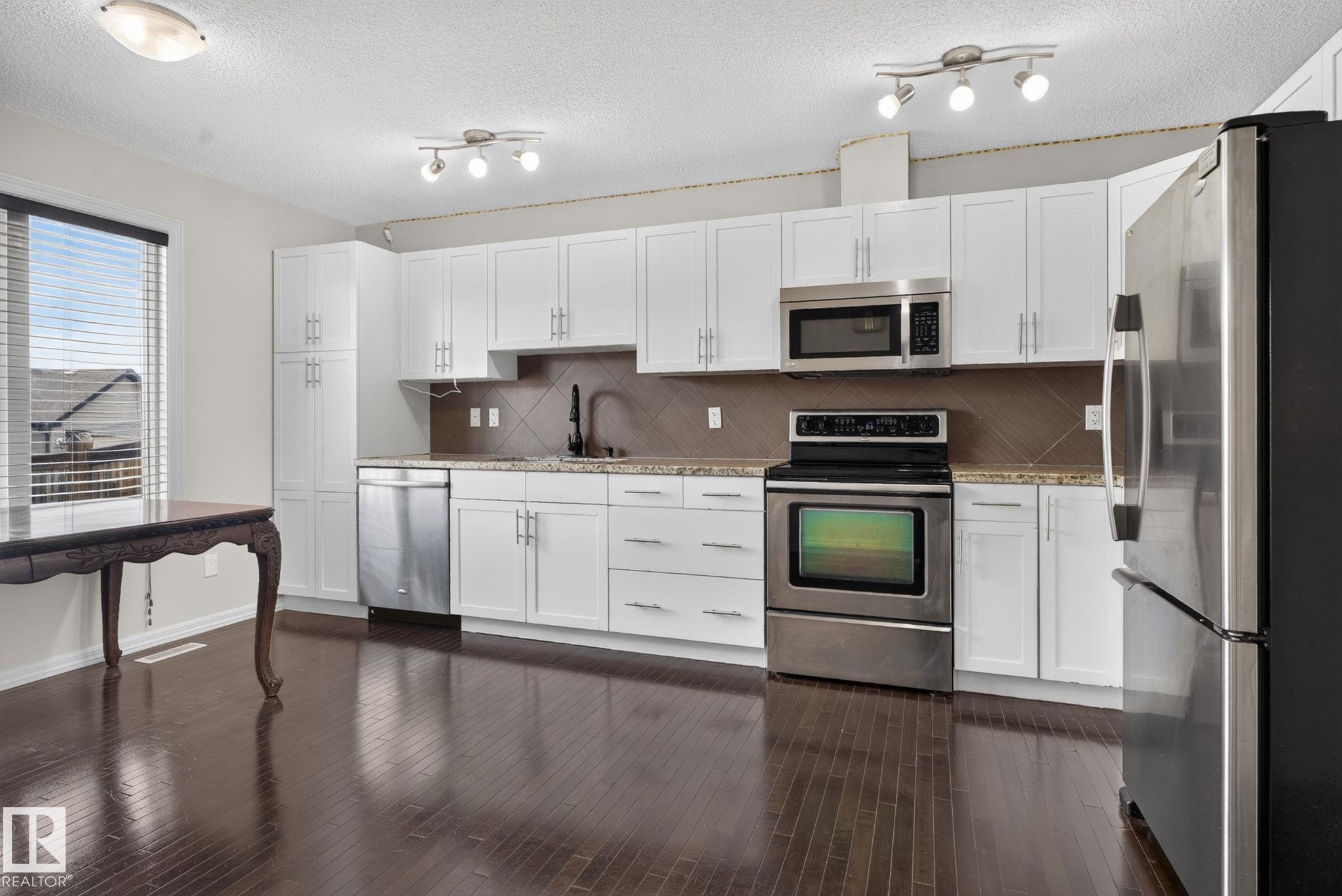 Kitchen featuring white cabinetry, stainless steel appliances, a tile backsplash, and wood-finish flooring - 545 Watt Boulevard Sw, Edmonton, AB - Indoor Photo Showing Kitchen With Stainless Steel Kitchen