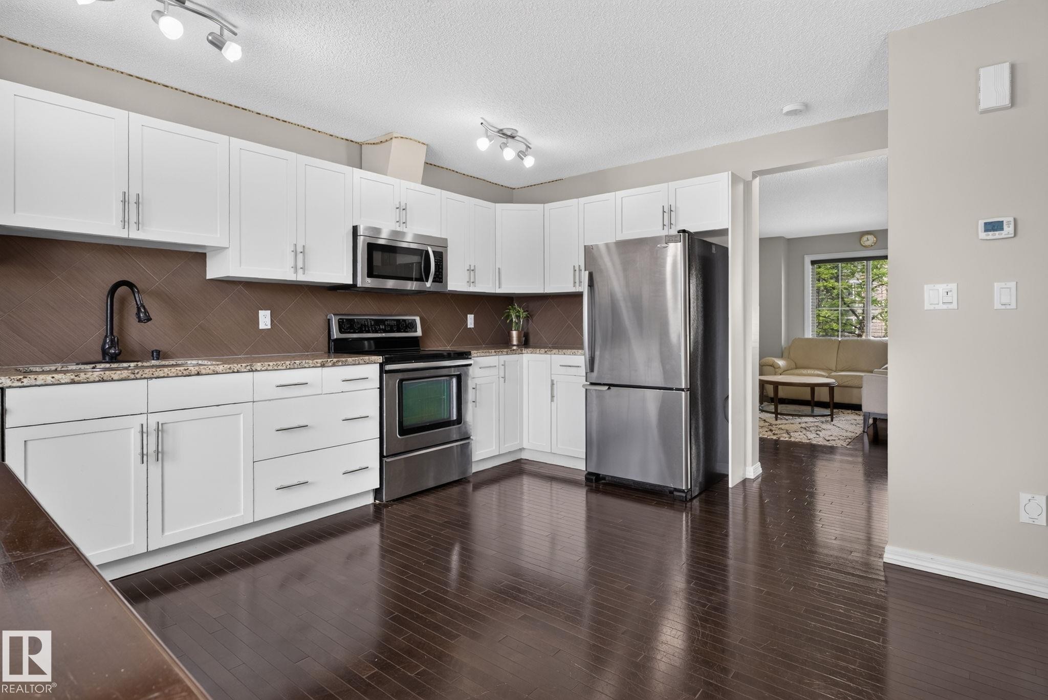 Modern kitchen featuring dark wood-finish flooring, white cabinetry, stainless steel appliances, a brown tiled backsplash, and light-toned countertops - 545 Watt Boulevard Sw, Edmonton, AB - Indoor Photo Showing Kitchen With Stainless Steel Kitchen