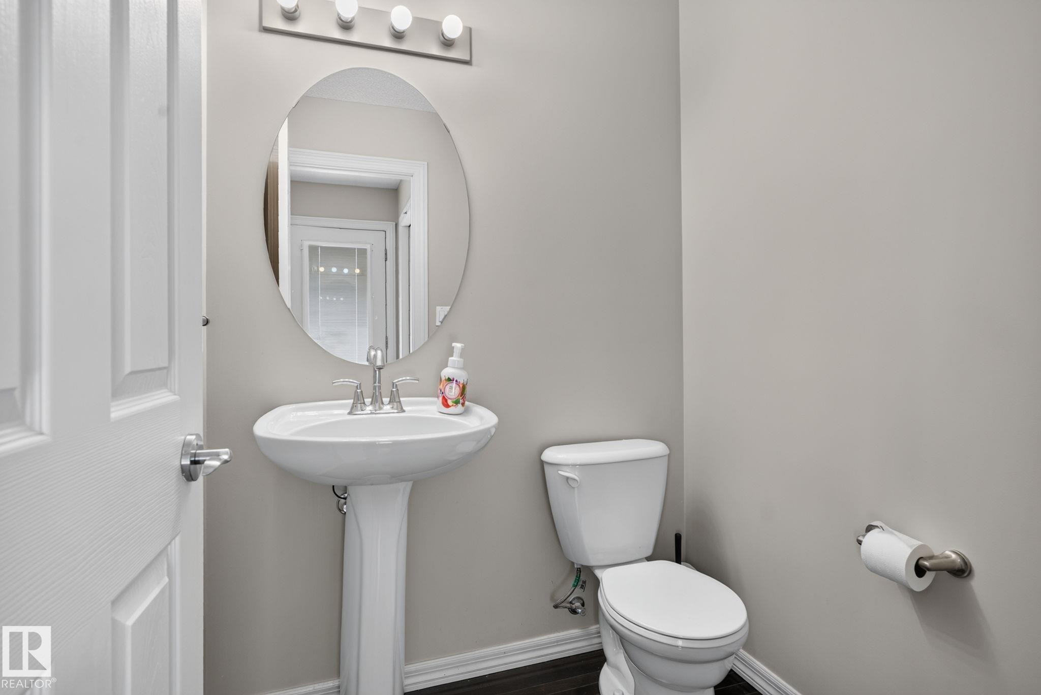 Powder room featuring a pedestal sink, oval mirror, brushed nickel hardware, and wood-finish flooring - 545 Watt Boulevard Sw, Edmonton, AB - Indoor Photo Showing Bathroom