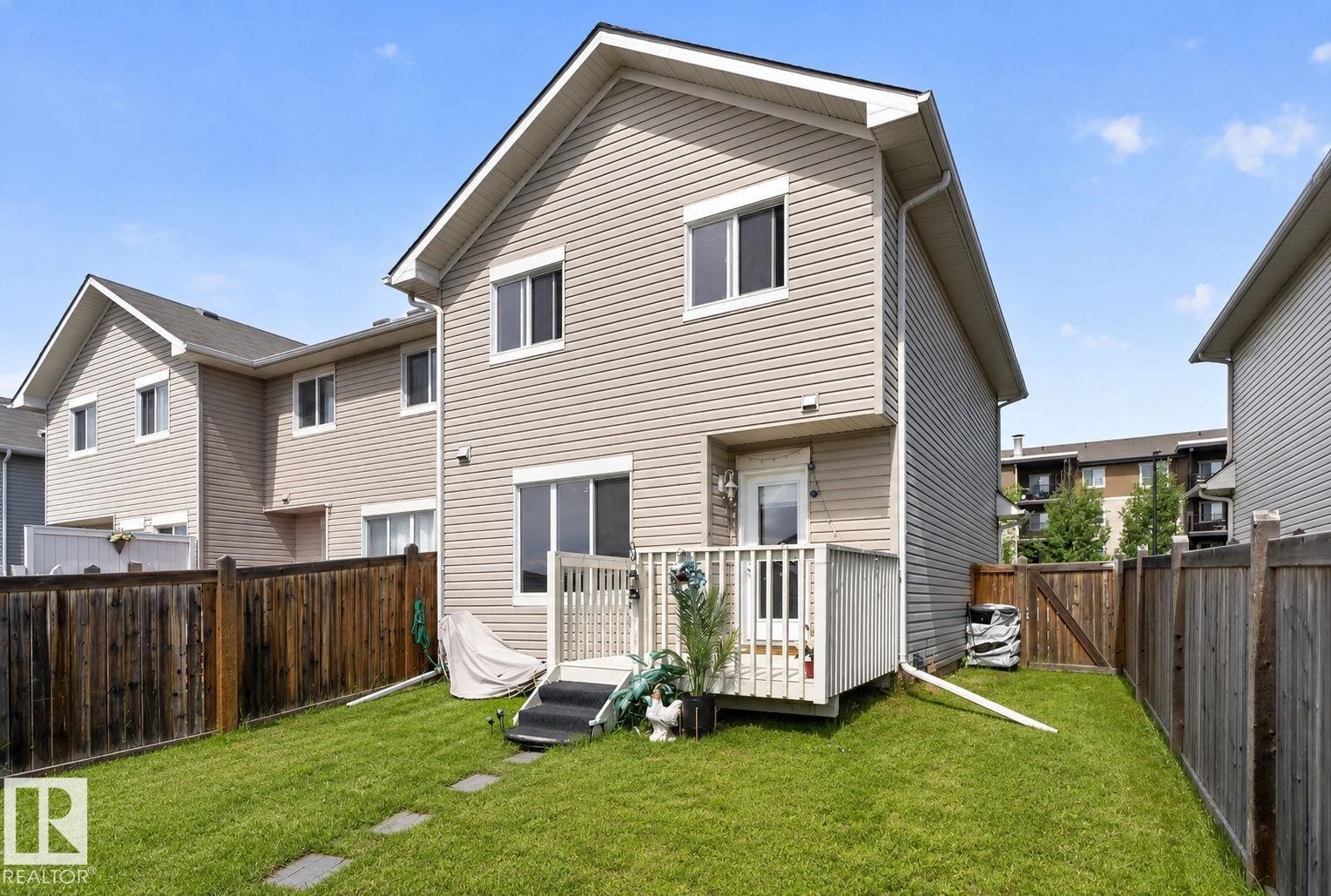 Rear exterior featuring neutral-toned siding, a wooden deck with white railings, and a manicured lawn - 545 Watt Boulevard Sw, Edmonton, AB - Outdoor With Exterior