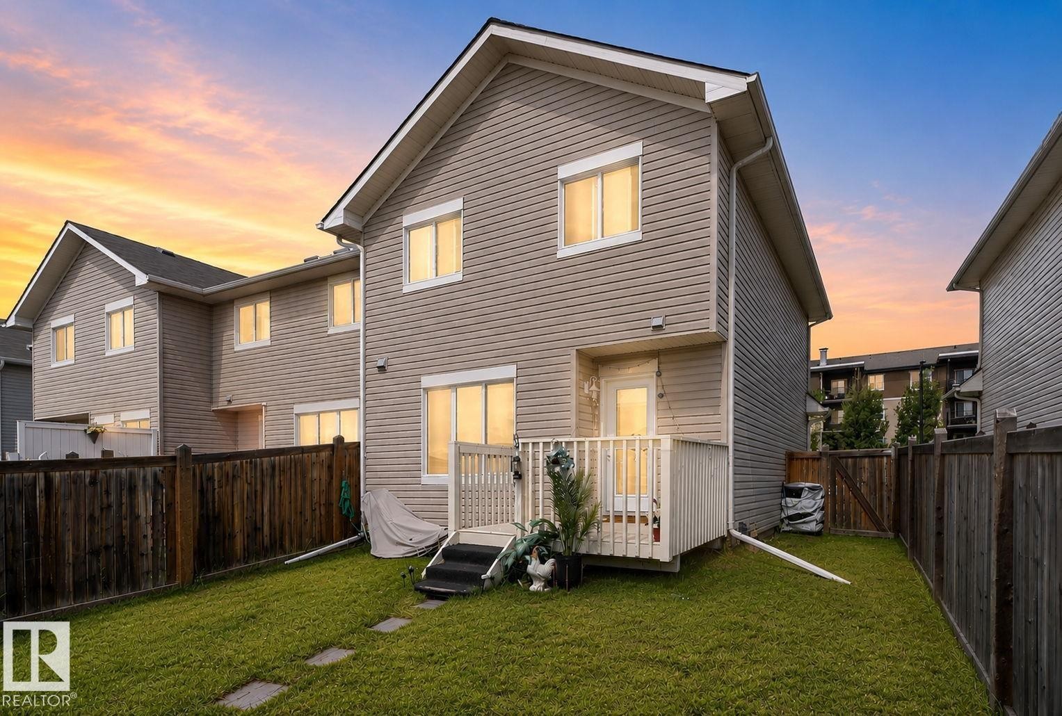 Rear exterior featuring tan horizontal siding, a private fenced yard with a grass lawn, and a back deck with white railings - 545 Watt Boulevard Sw, Edmonton, AB - Outdoor With Exterior