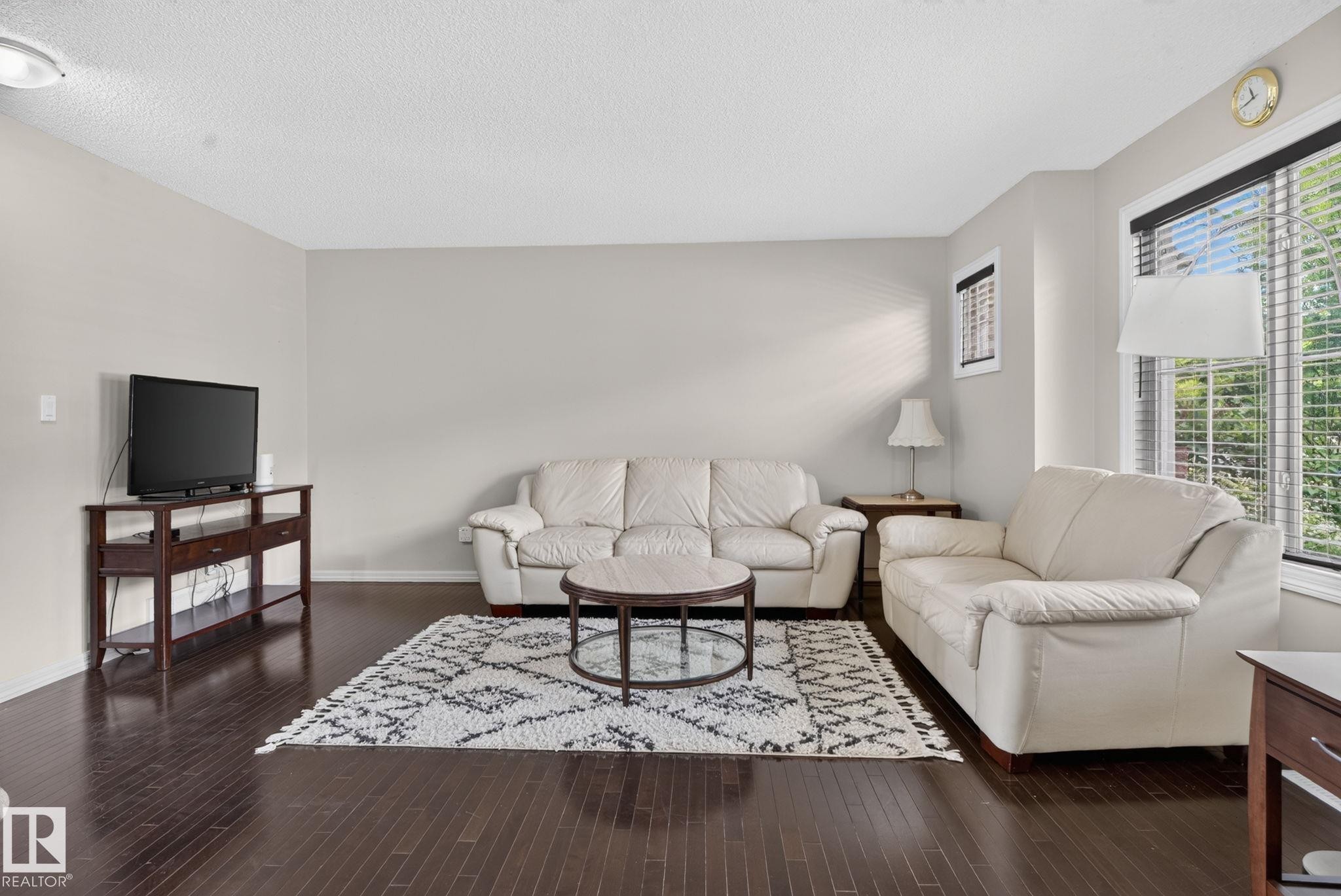 Spacious living area featuring dark wood-finish flooring, light neutral wall tones, and a large window with horizontal blinds - 545 Watt Boulevard Sw, Edmonton, AB - Indoor Photo Showing Living Room