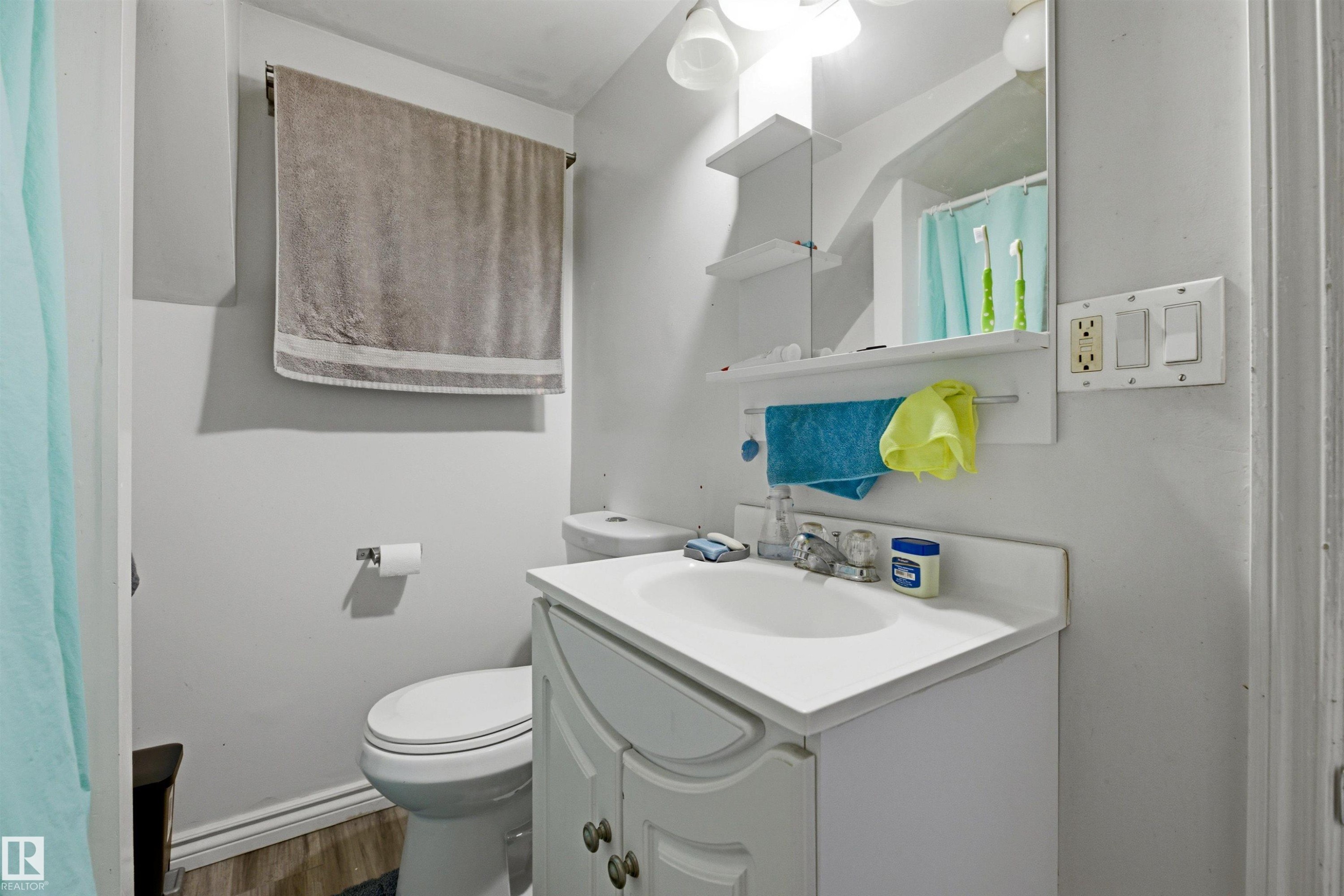 Bathroom featuring a white vanity with integrated sink, wood-finish flooring, and wall-mounted mirror with integrated shelving - 8911 169 Street Nw, Edmonton, AB - Indoor Photo Showing Bathroom