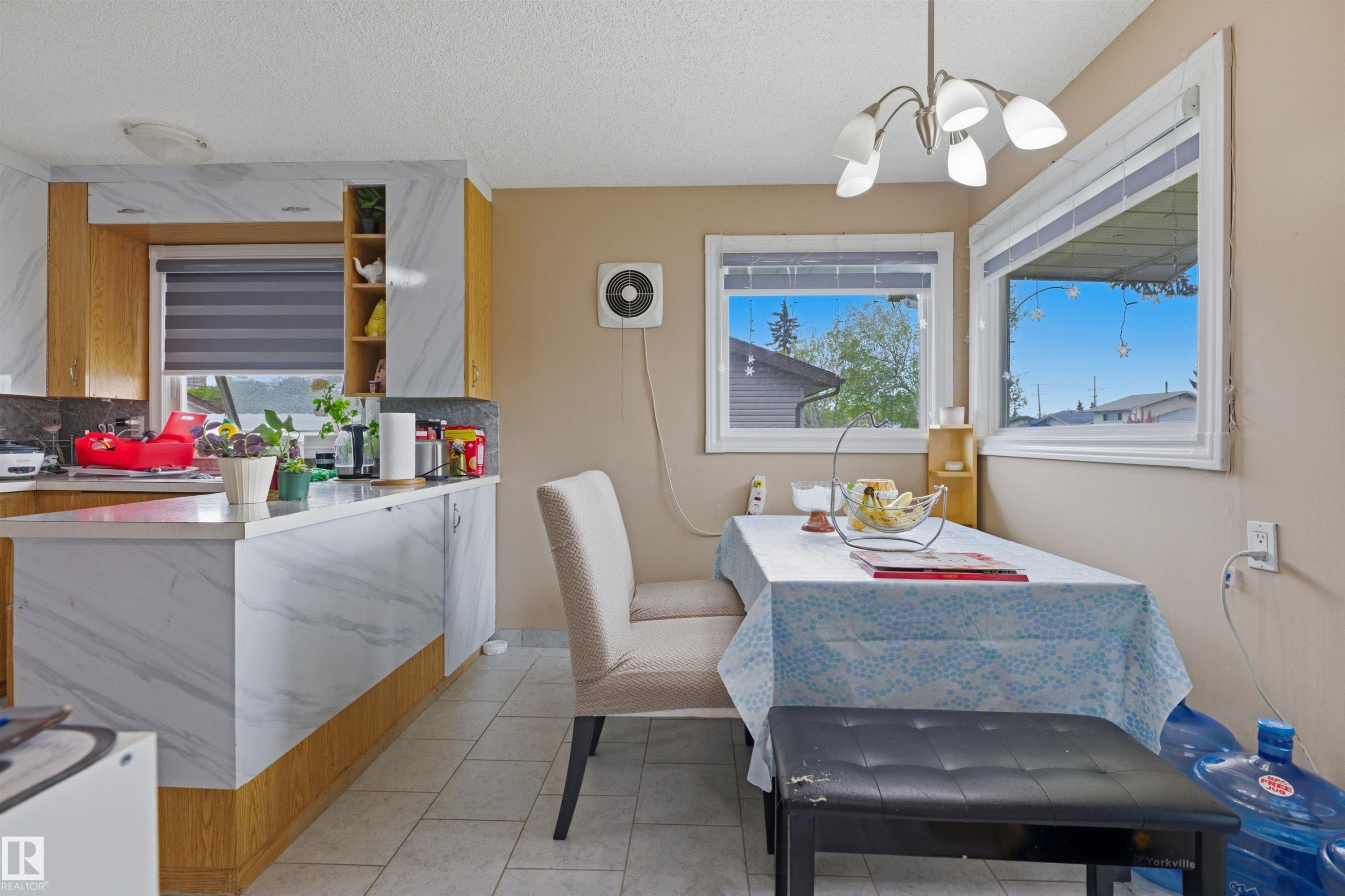 Kitchen and dining area featuring wood-finish cabinetry with white and grey marbled surfaces, white tile flooring, and a multi-light ceiling fixture - 8911 169 Street Nw, Edmonton, AB - Indoor