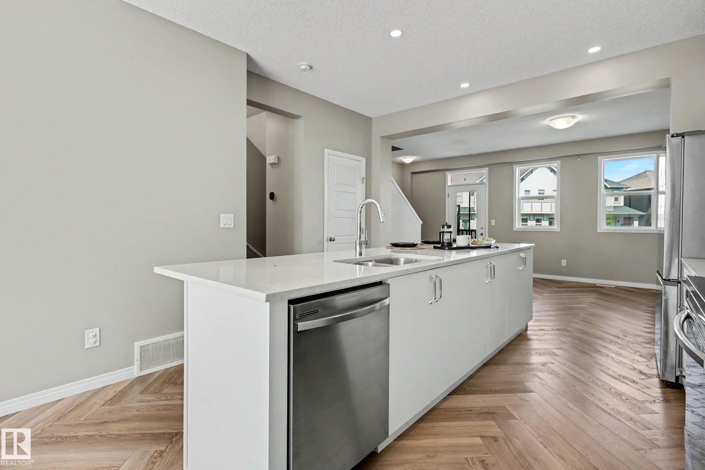 Kitchen island featuring a stainless steel dishwasher, an undermount sink with a gooseneck faucet, and a light-toned countertop - 53 2072 Wonnacott Way, Edmonton, AB