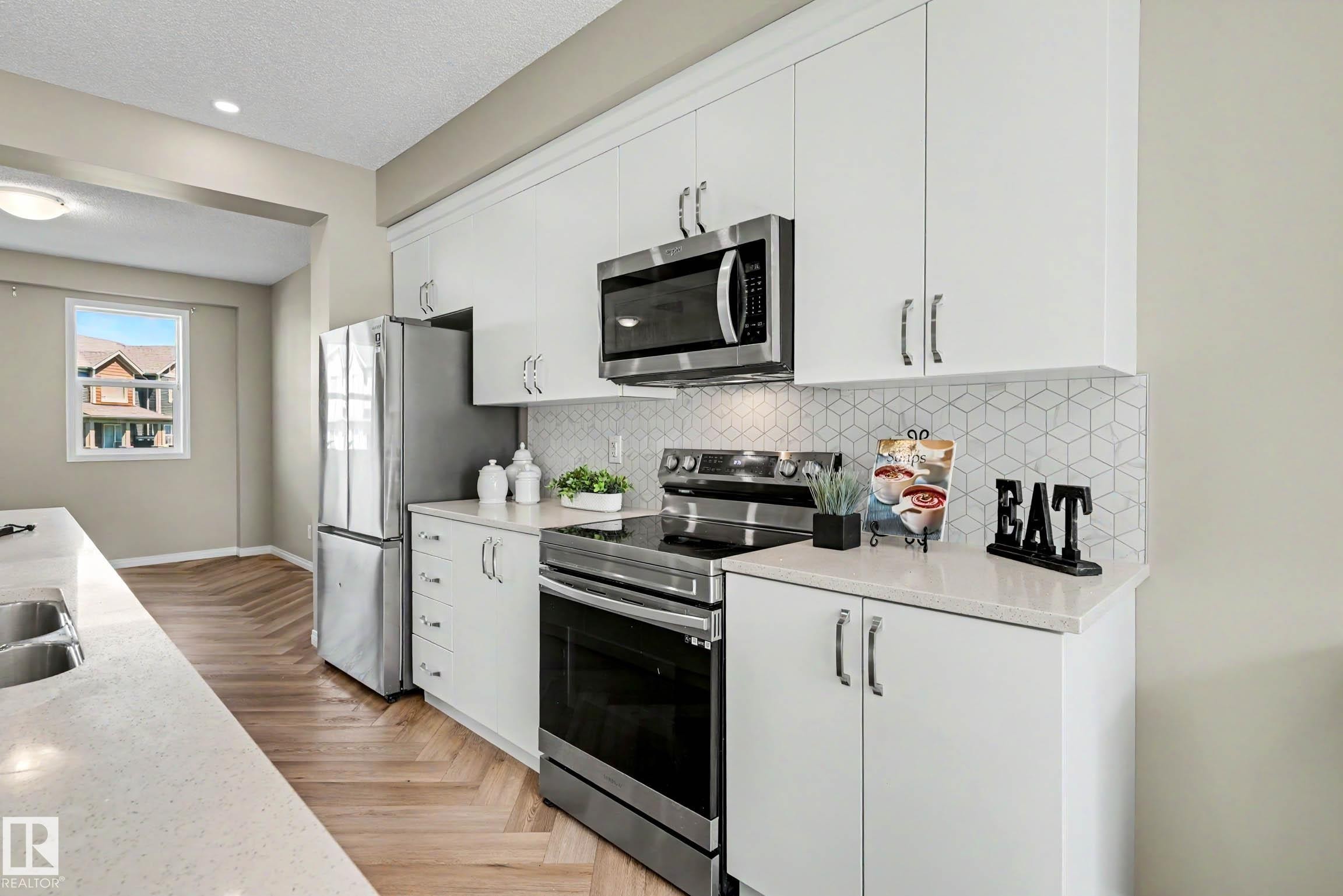Kitchen featuring white cabinetry, stainless steel appliances, a geometric tile backsplash, light-toned countertops, and wood-finish flooring - 53 2072 Wonnacott Way, Edmonton, AB