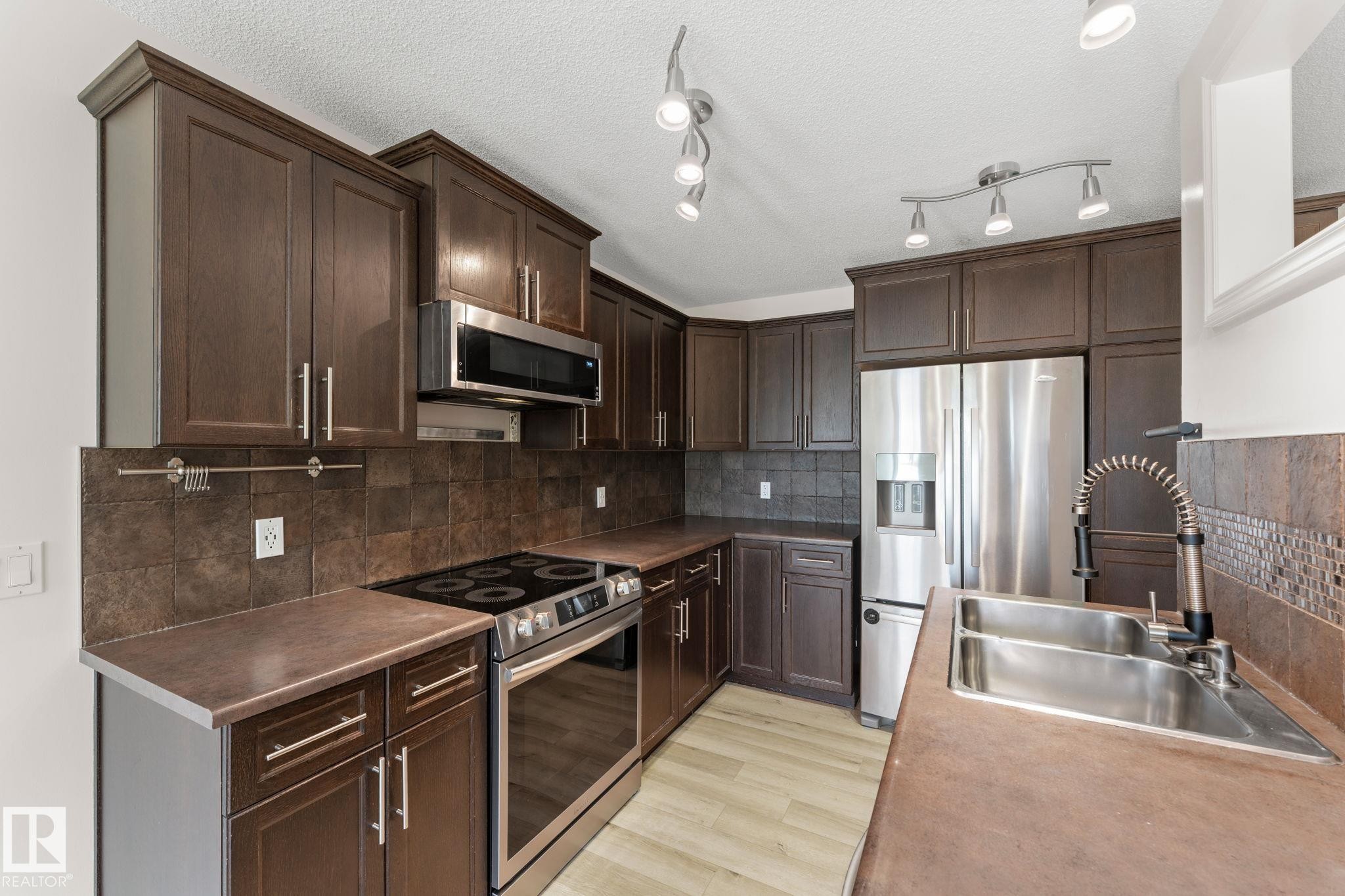 Kitchen featuring dark wood-finish cabinetry, stainless steel appliances, a tile backsplash, and light wood-finish flooring - 12523 171 Avenue, Edmonton, AB