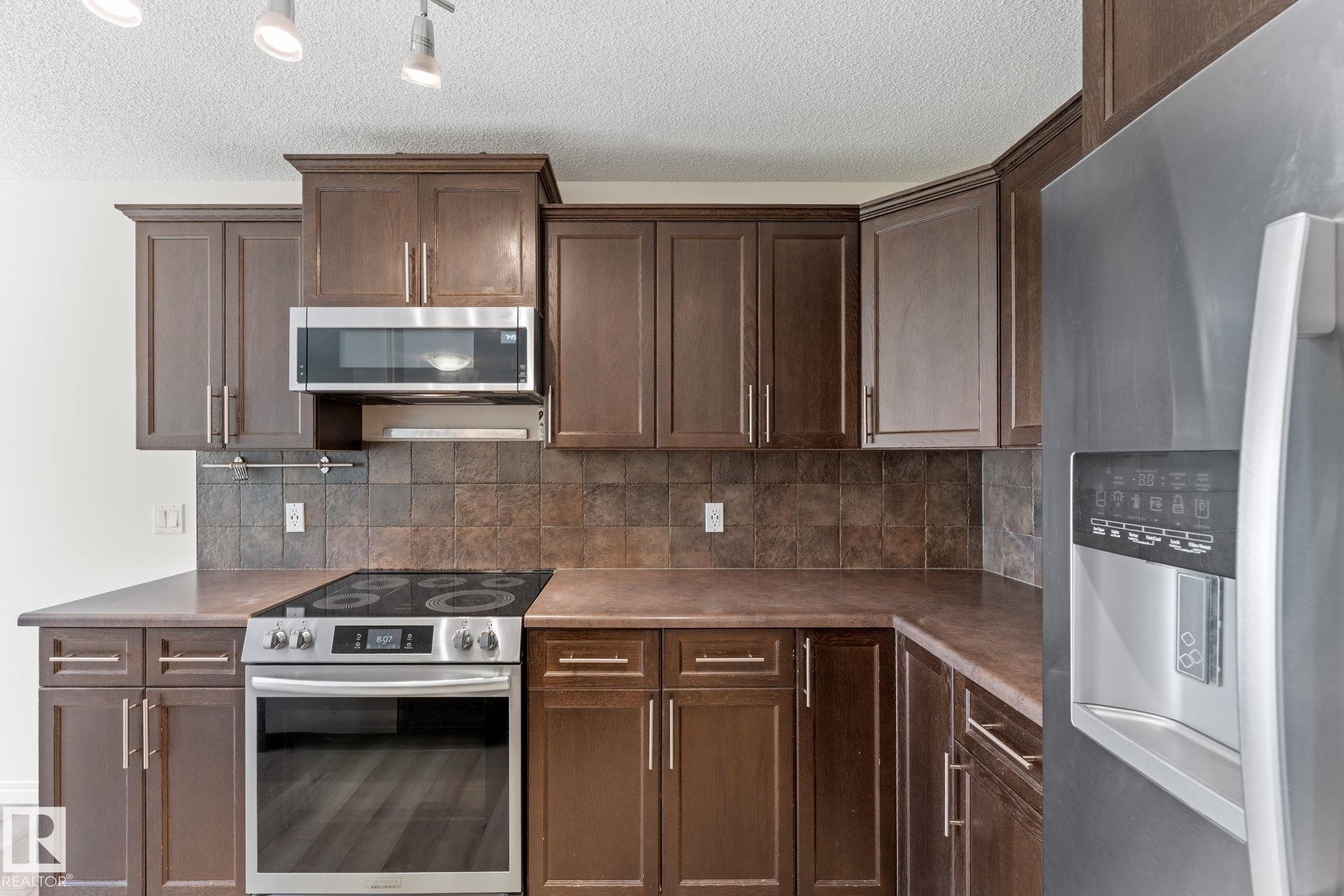 Modern kitchen featuring wood-finish cabinetry, stainless steel appliances, and a tiled backsplash - 12523 171 Avenue, Edmonton, AB