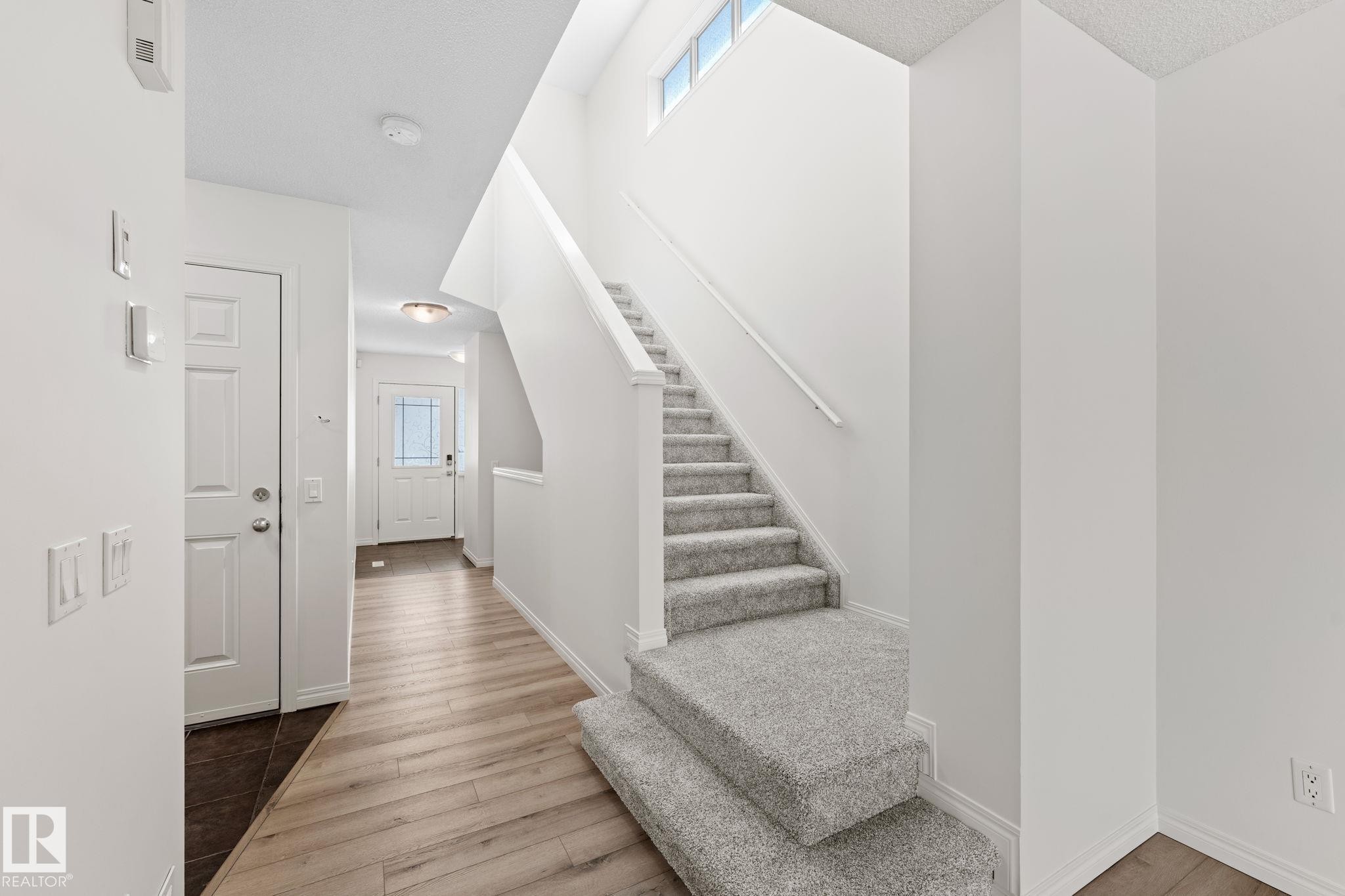 Foyer featuring a light wood-finish flooring, a white paneled door, and a staircase with light grey carpeting and a handrail - 12523 171 Avenue, Edmonton, AB