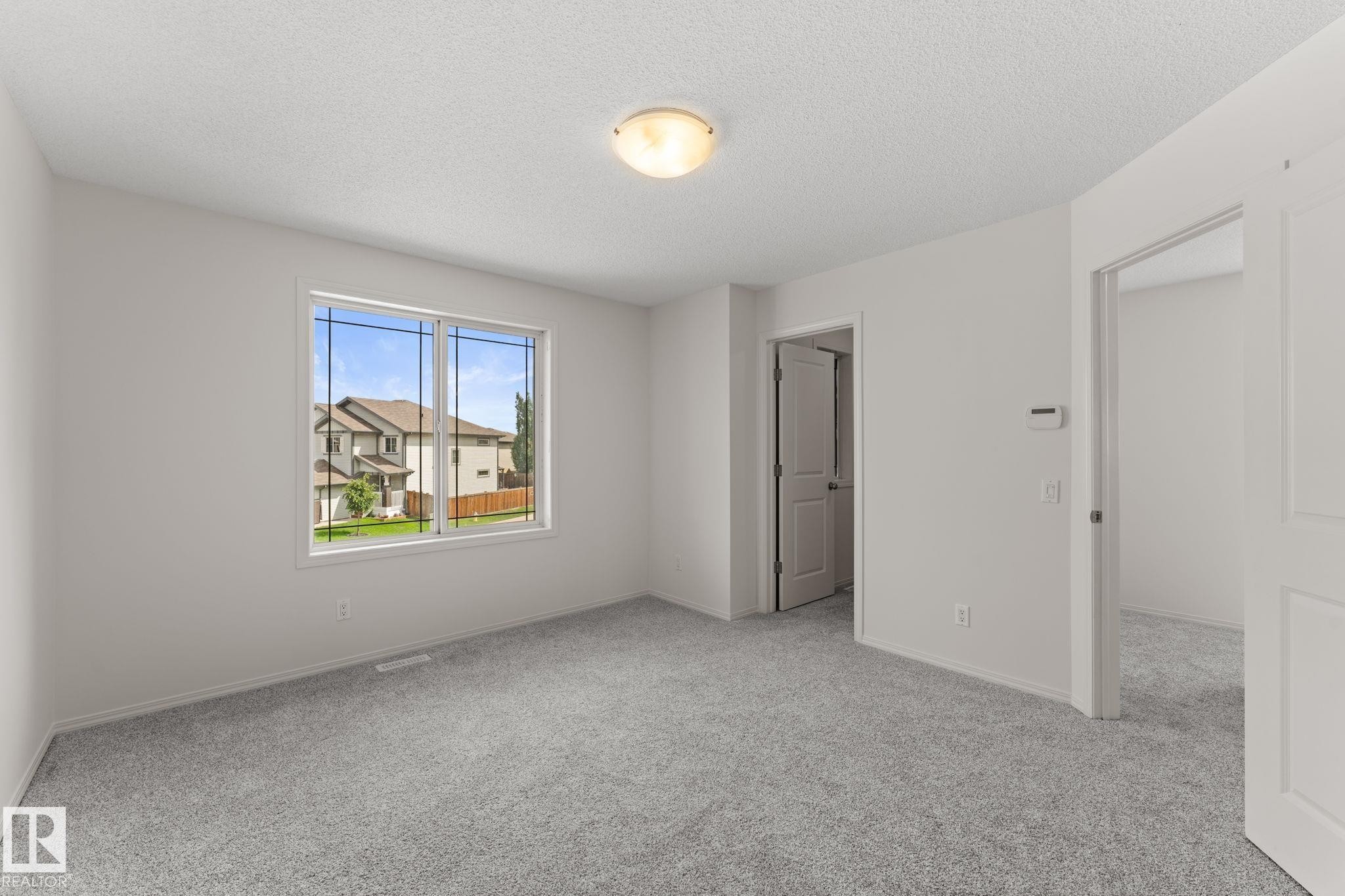 Bright interior room featuring a large window, light gray carpeting, and fresh white walls - 12523 171 Avenue, Edmonton, AB