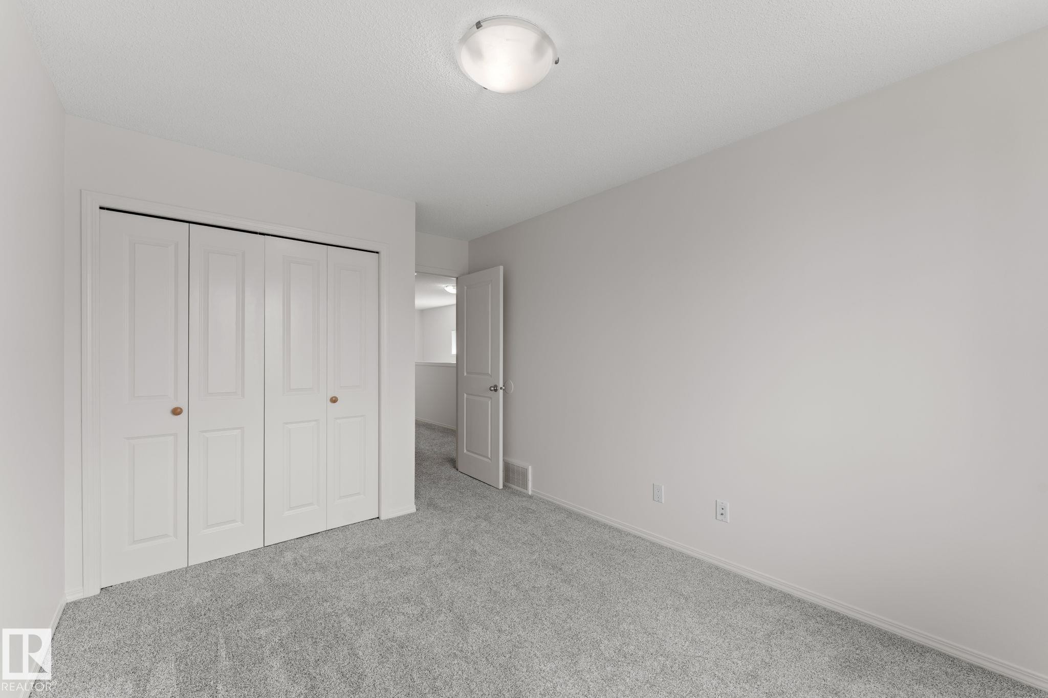 Bedroom featuring light gray carpeting, white walls, a flush-mount ceiling light fixture, and bifold closet doors with round wooden knobs - 12523 171 Avenue, Edmonton, AB