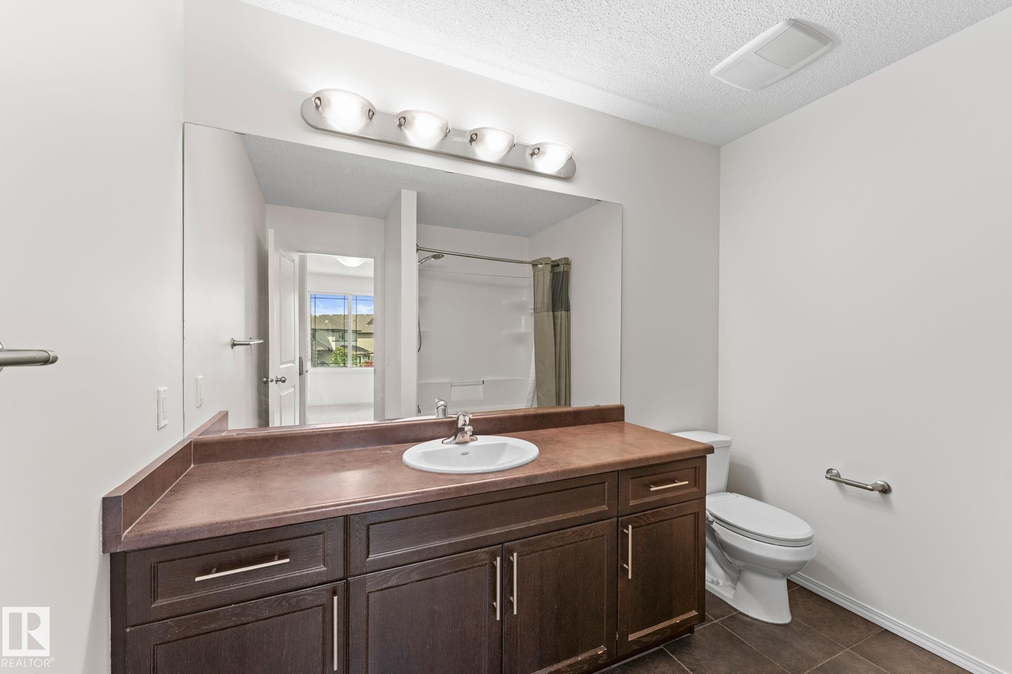 Bathroom featuring a dark wood-finish vanity with a single basin sink, large wall-mounted mirror, and overhead lighting fixture - 12523 171 Avenue, Edmonton, AB