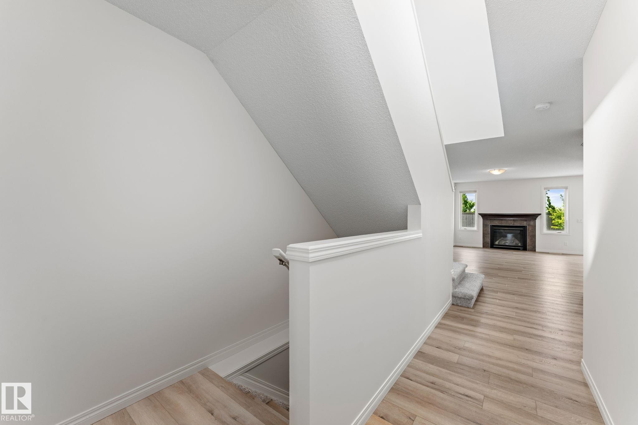 Hallway featuring wood-finish flooring, white baseboards, and a partial carpeted staircase - 12523 171 Avenue, Edmonton, AB
