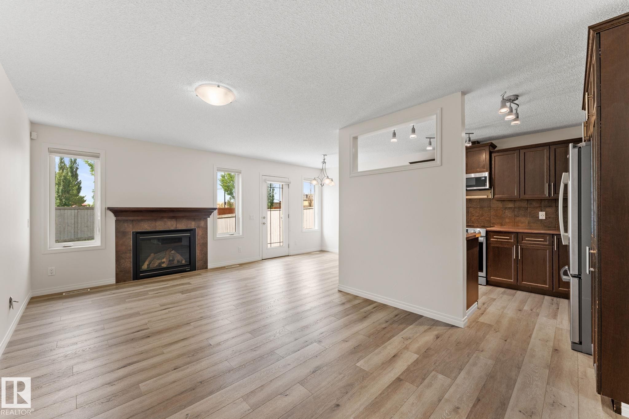 Spacious living area featuring wood-finish flooring, a fireplace with a stone surround, and multiple windows - 12523 171 Avenue, Edmonton, AB
