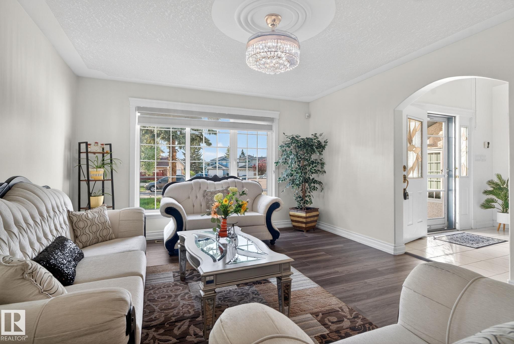 Spacious living area featuring wood-finish flooring, a large window, and an elegant chandelier with a ceiling medallion - 4615 43A Avenue, Edmonton, AB - Indoor Photo Showing Living Room