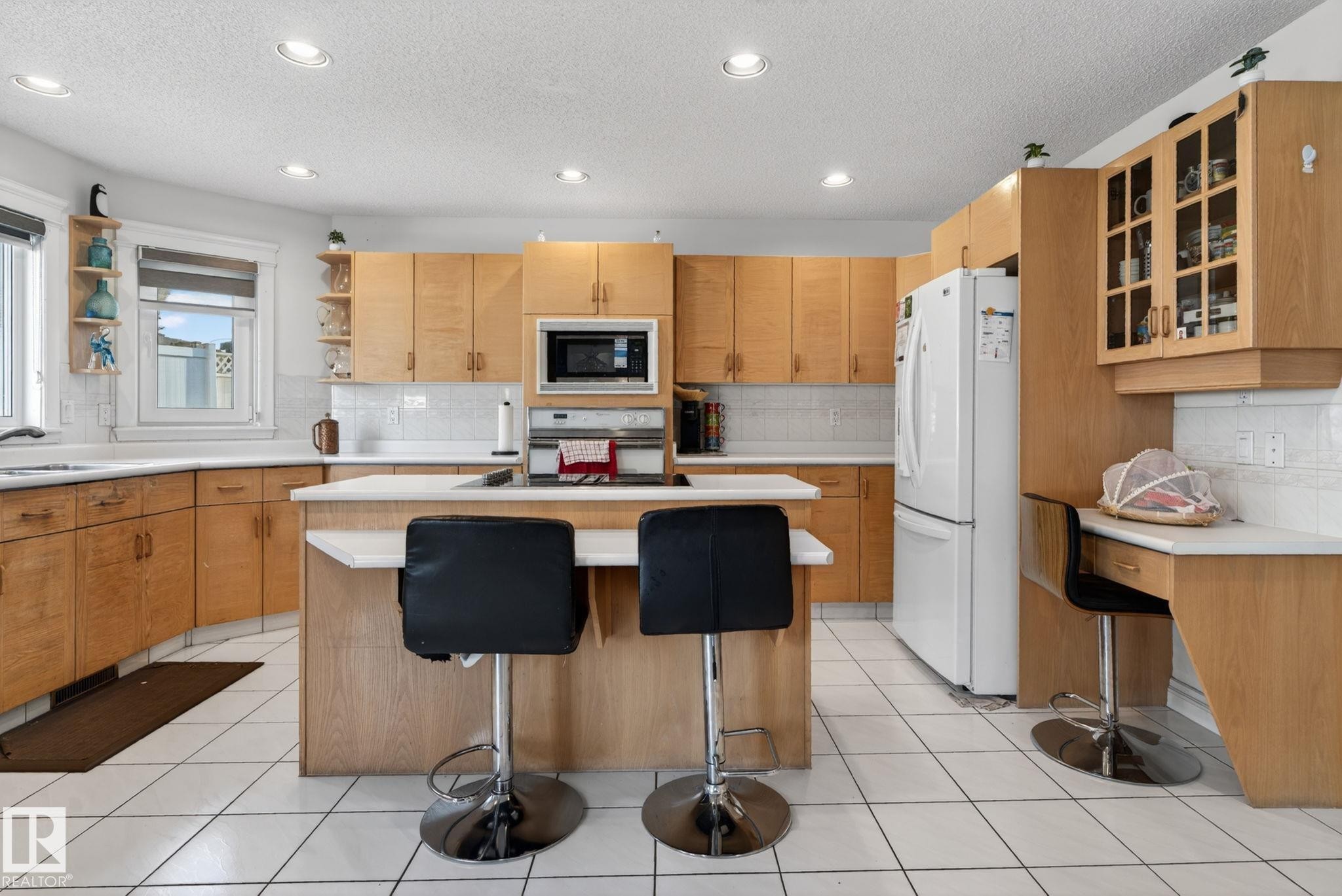 Kitchen featuring wood cabinetry, white tile flooring, white countertops, built-in microwave, and a central island with breakfast bar seating - 4615 43A Avenue, Edmonton, AB - Indoor Photo Showing Kitchen