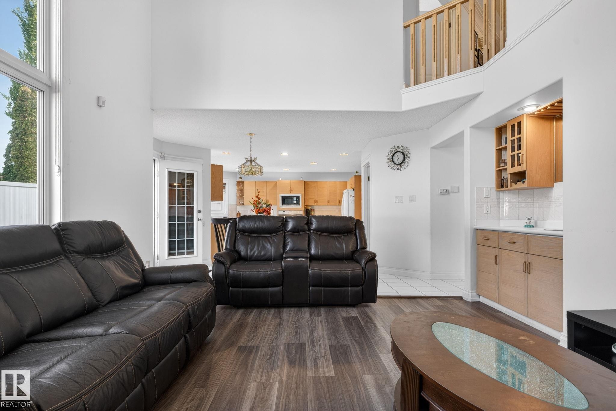 Vaulted ceilings highlight the living area, featuring wood-finish flooring, a built-in wet bar with cabinetry, and an upper-level balcony with a wood railing - 4615 43A Avenue, Edmonton, AB - Indoor Photo Showing Living Room