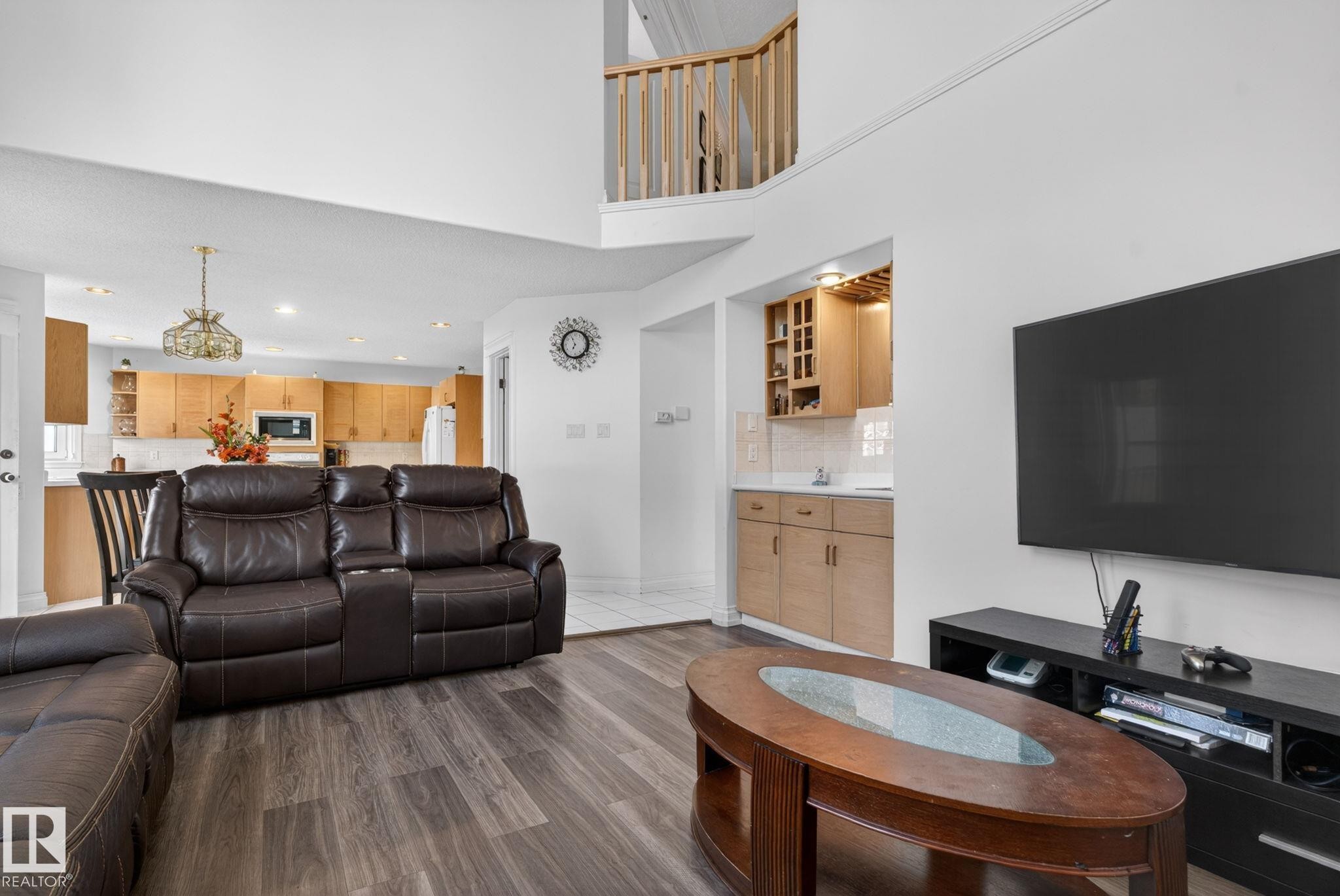 Open-concept living area featuring wood-finish flooring, a built-in wet bar with light wood cabinetry, and a kitchen with light wood cabinetry and a decorative chandelier - 4615 43A Avenue, Edmonton, AB - Indoor Photo Showing Living Room