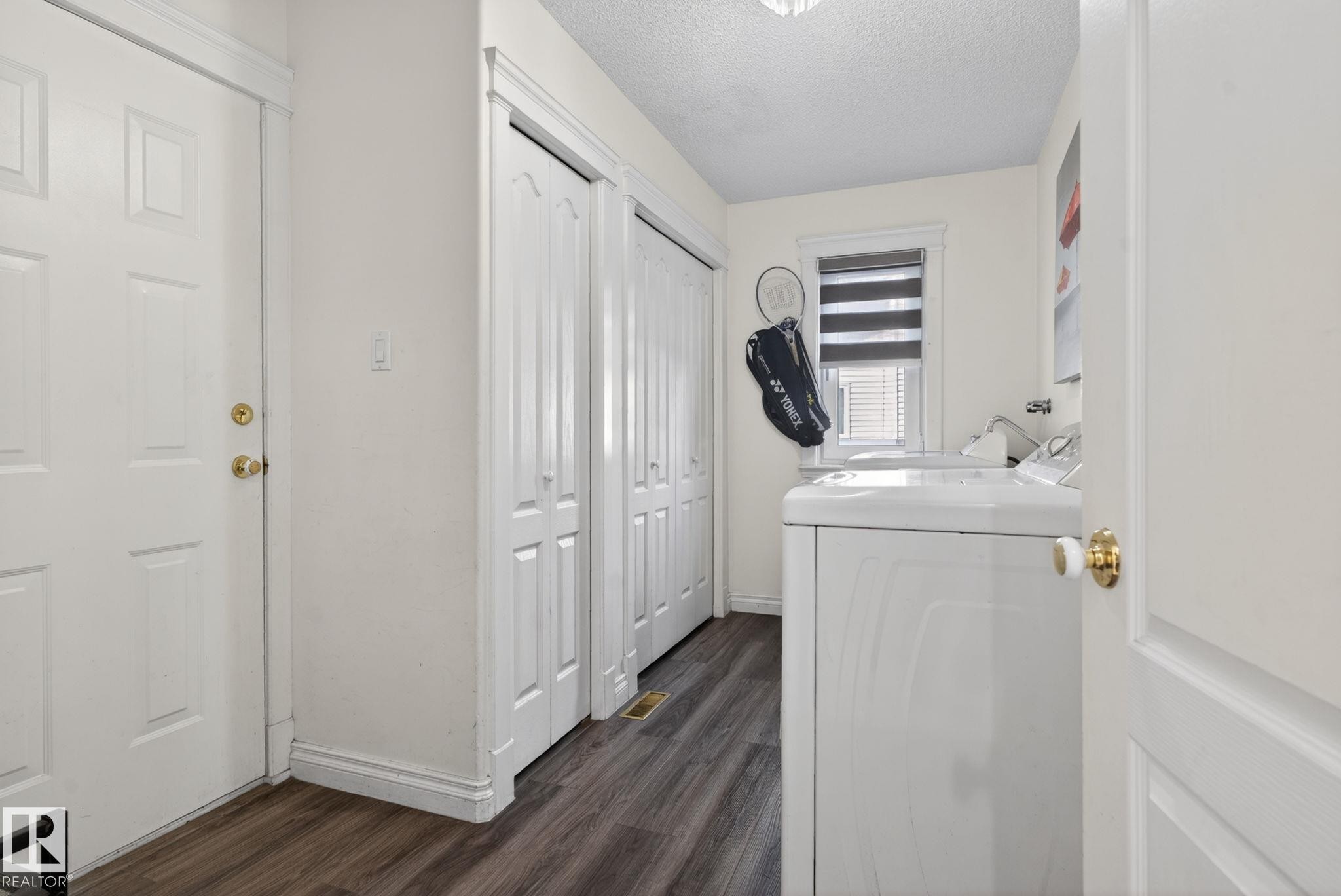 Dedicated laundry area featuring wood-finish flooring, a white paneled door with brass hardware, and built-in bifold closet doors - 4615 43A Avenue, Edmonton, AB - Indoor Photo Showing Laundry Room