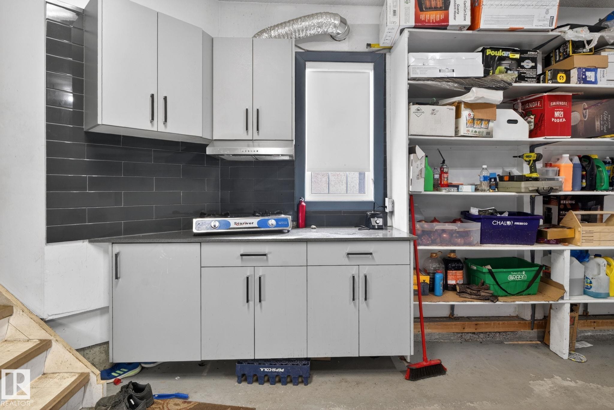 Compact kitchen area featuring light gray cabinetry with black hardware, a dark countertop, and a dark tile backsplash - 4615 43A Avenue, Edmonton, AB - Indoor