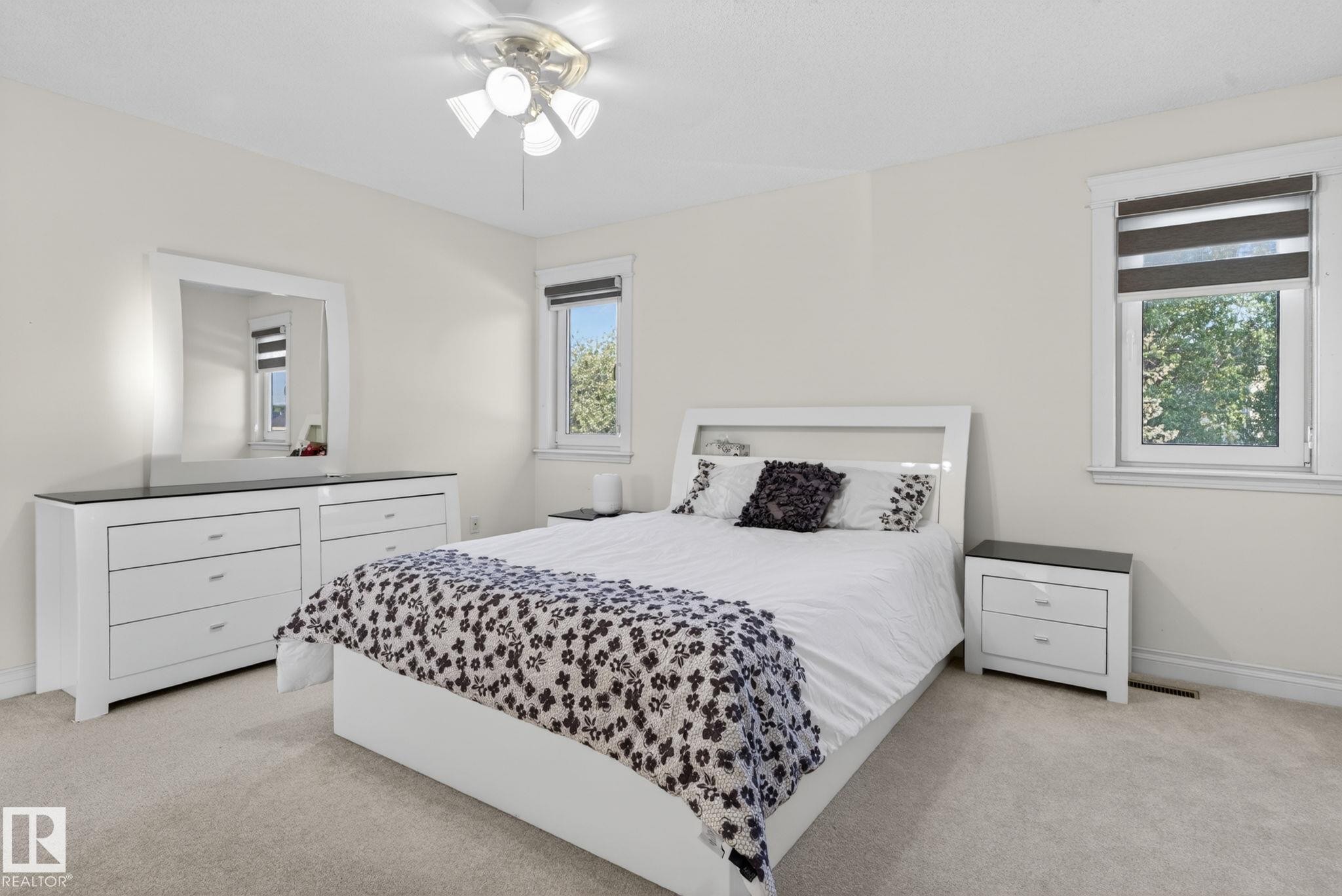 Carpeted bedroom featuring neutral wall paint, two windows with roller blinds, and a ceiling fan with integrated lighting - 4615 43A Avenue, Edmonton, AB - Indoor Photo Showing Bedroom