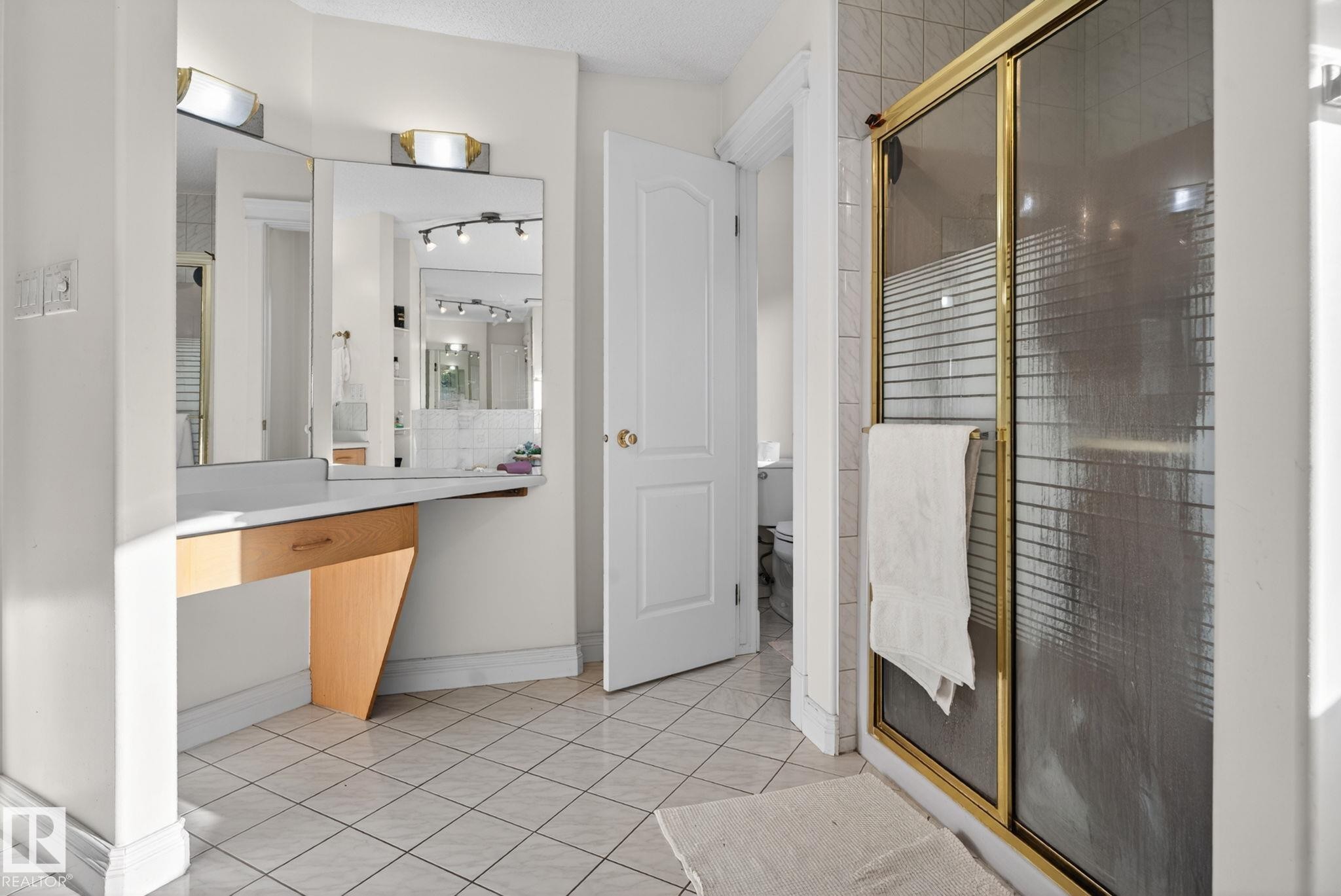 Tiled bathroom featuring a vanity area with dual mirrors, integrated lighting, and a built-in drawer - 4615 43A Avenue, Edmonton, AB - Indoor