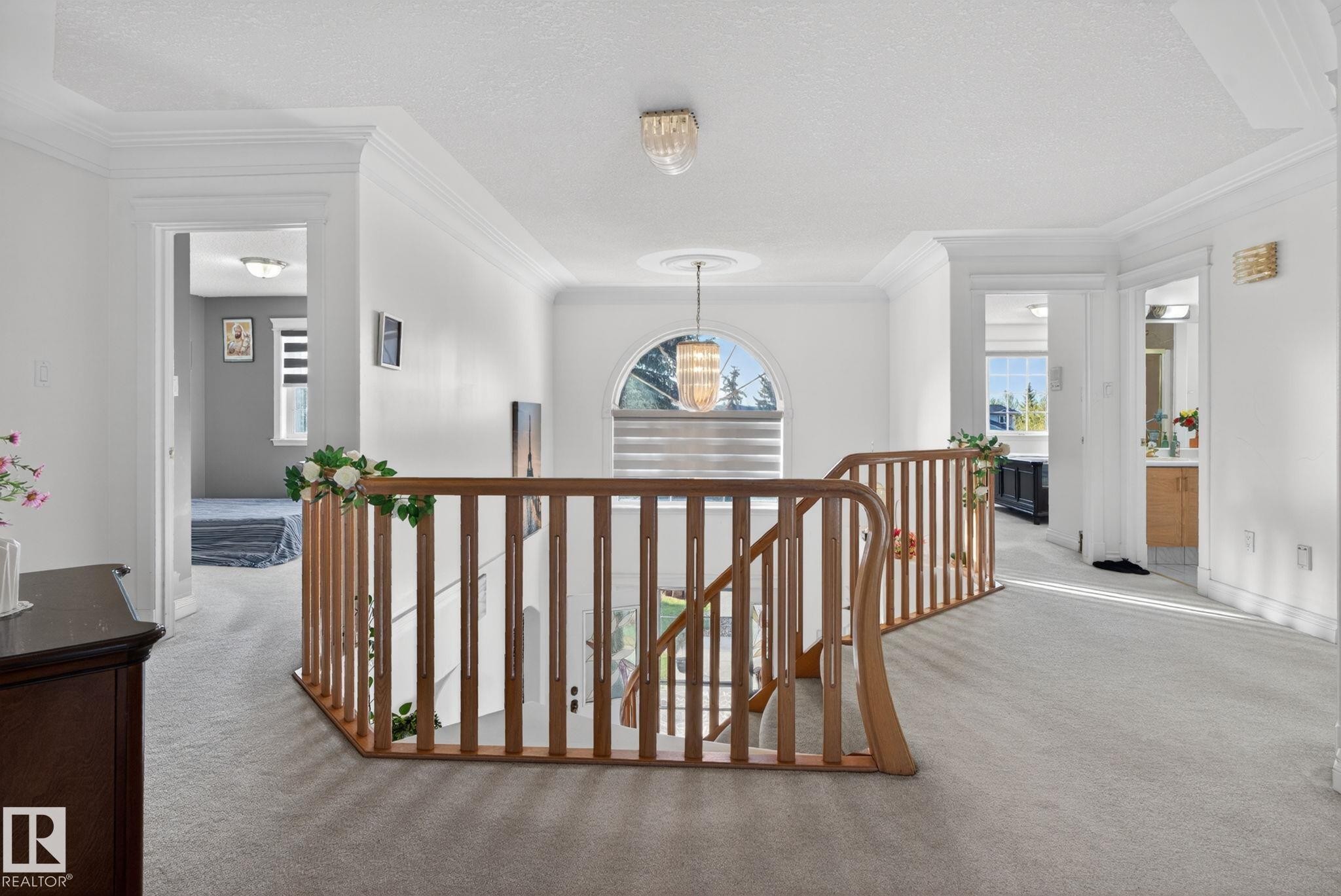 Spacious upper landing featuring light-toned carpeting, a wood-finish staircase railing, and an arched window - 4615 43A Avenue, Edmonton, AB - Indoor Photo Showing Other Room