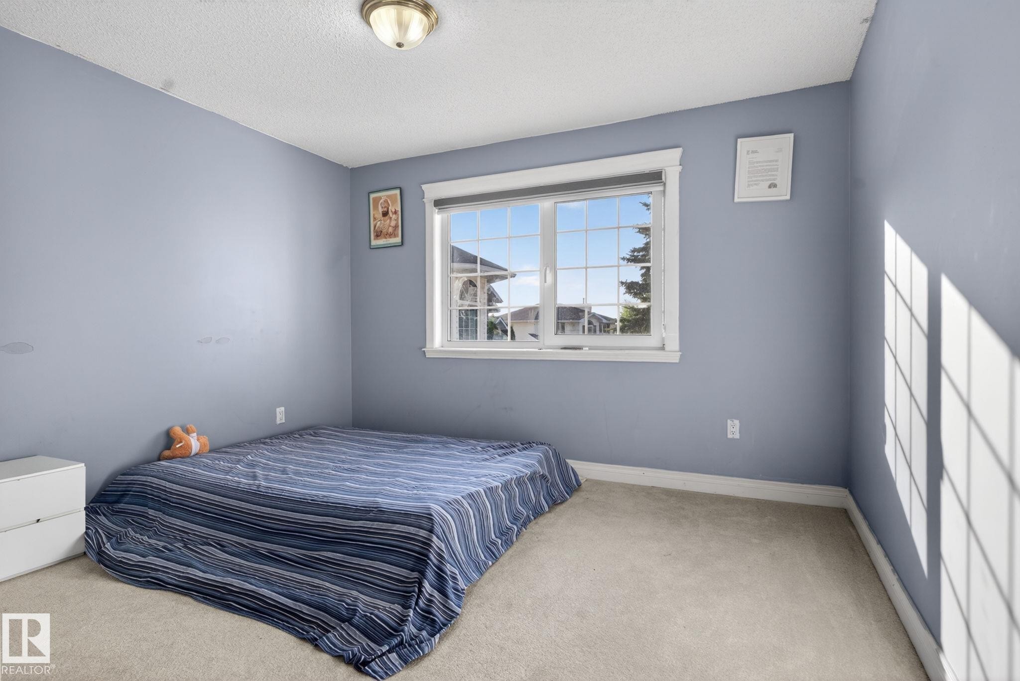 Spacious room featuring a large window with white trim, light blue walls, textured ceiling, and carpeted flooring - 4615 43A Avenue, Edmonton, AB - Indoor Photo Showing Bedroom