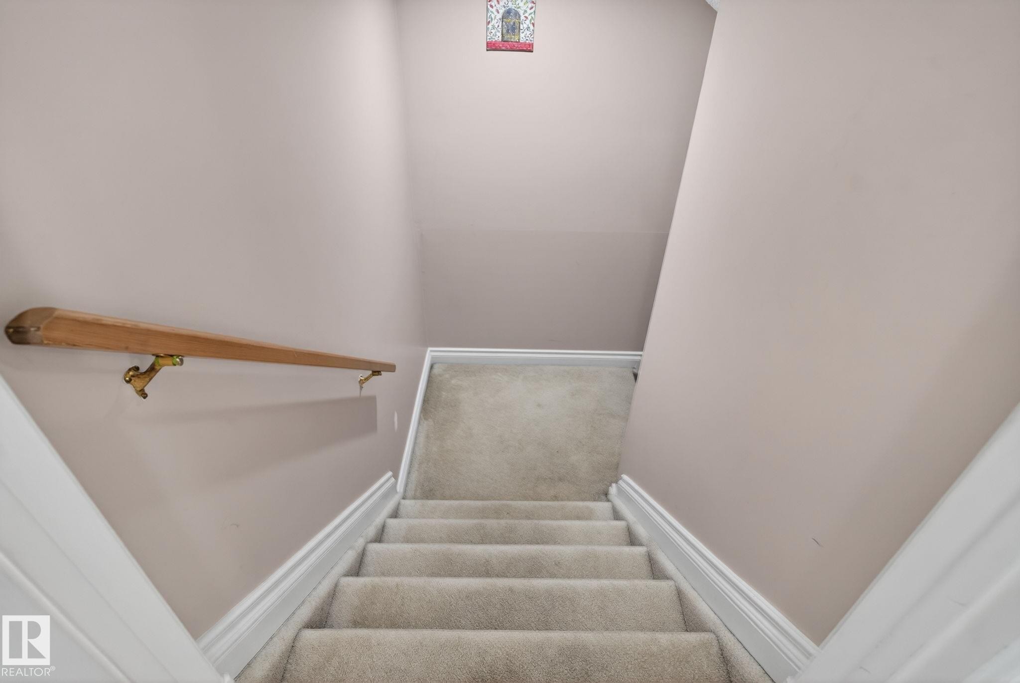 Carpeted staircase with light-toned wall paint, white trim, and a wood handrail with brass-toned brackets - 4615 43A Avenue, Edmonton, AB - Indoor Photo Showing Other Room