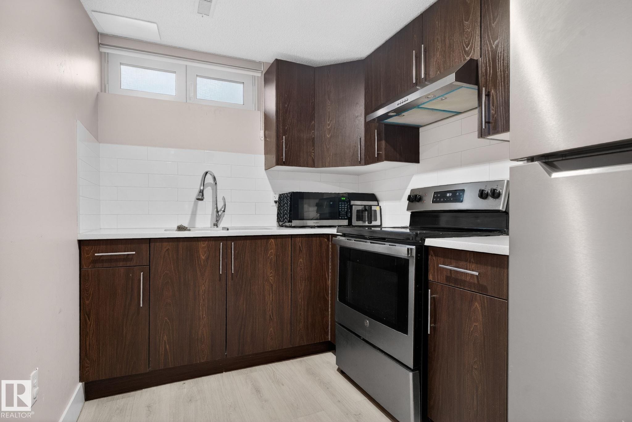 Kitchen featuring dark wood-finish cabinetry, light countertops, white subway tile backsplash, stainless steel appliances, and a window above the sink - 4615 43A Avenue, Edmonton, AB - Indoor Photo Showing Kitchen