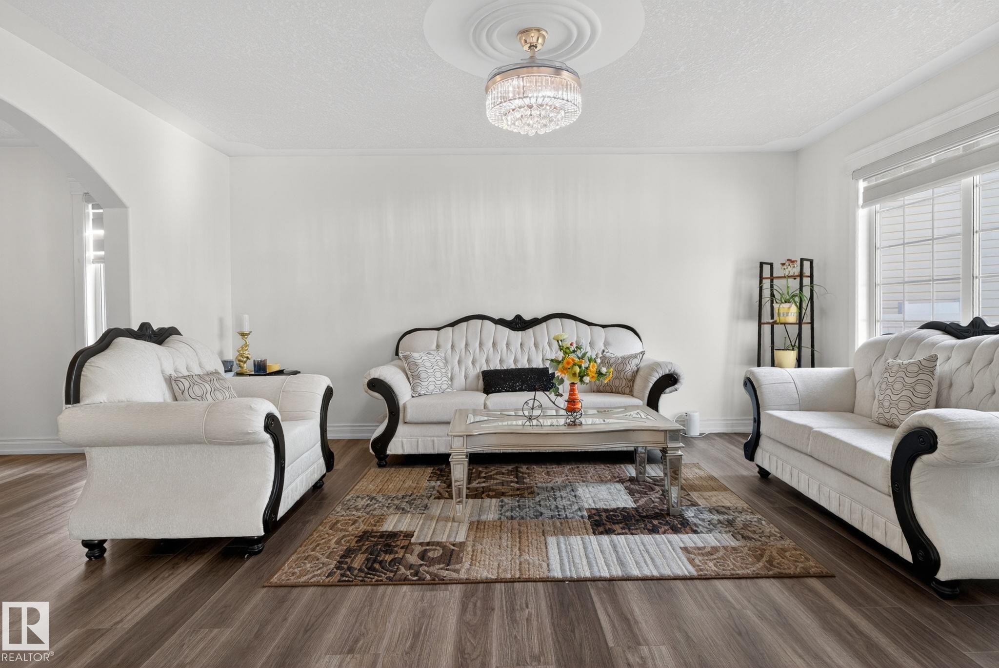 Spacious living area featuring wood-finish flooring, white painted walls, crown molding, and an elegant crystal chandelier with a ceiling medallion - 4615 43A Avenue, Edmonton, AB - Indoor Photo Showing Living Room