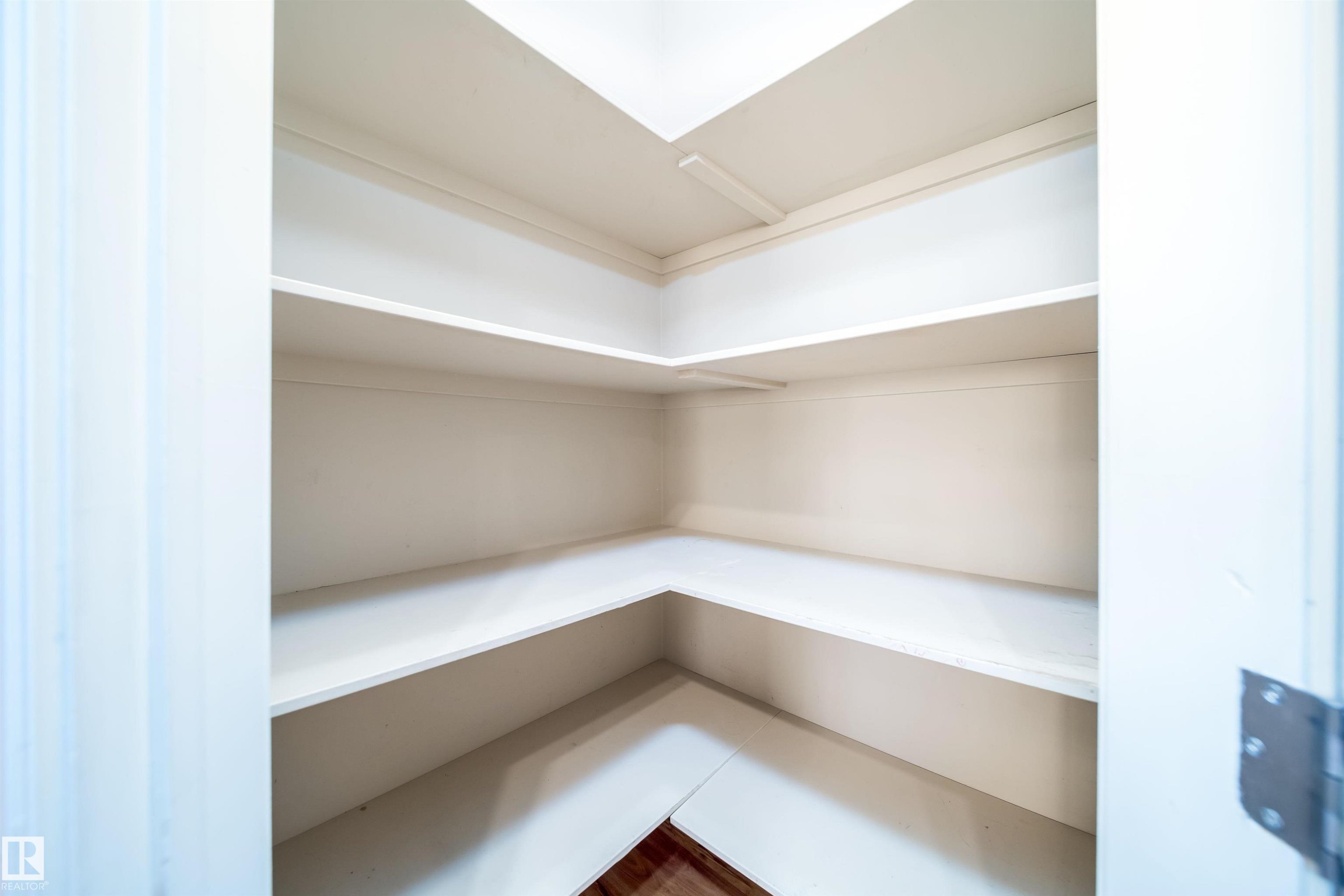 Corner pantry with multiple white shelves and wood-finish flooring - #46 15151 43 St Nw, Edmonton, AB - Indoor With Storage