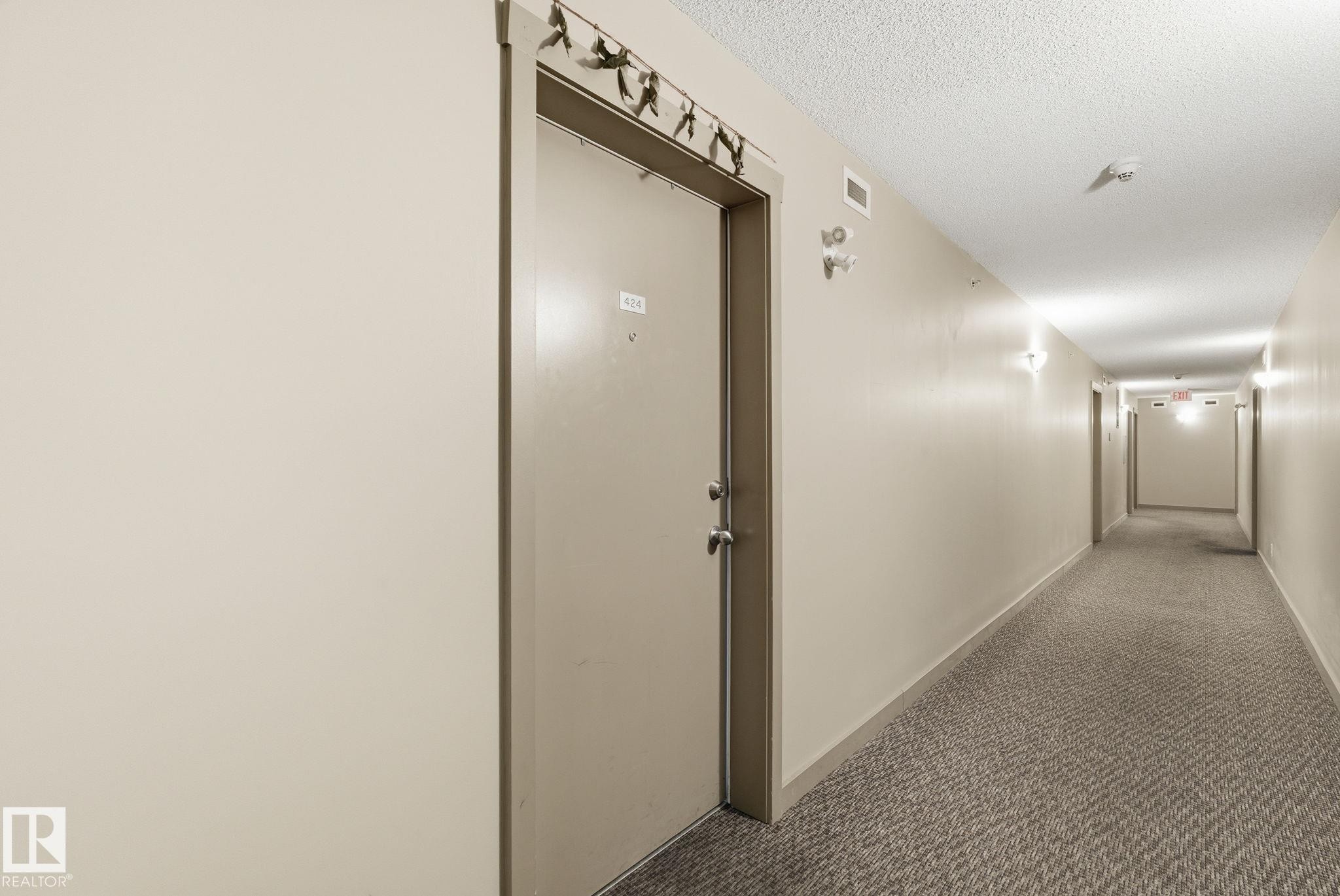 Long hallway with textured carpeting, cream-painted walls, and ceiling-mounted light fixtures - 424 1510 Watt Drive, Edmonton, AB
