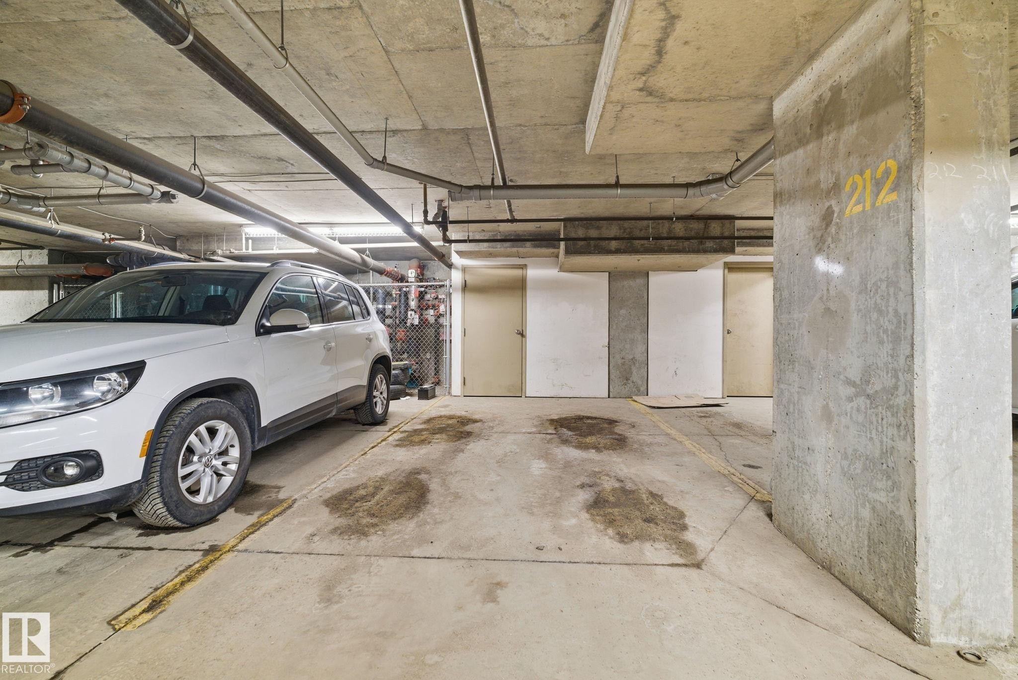 Concrete parking garage featuring exposed overhead piping and fluorescent lighting - 424 1510 Watt Drive, Edmonton, AB
